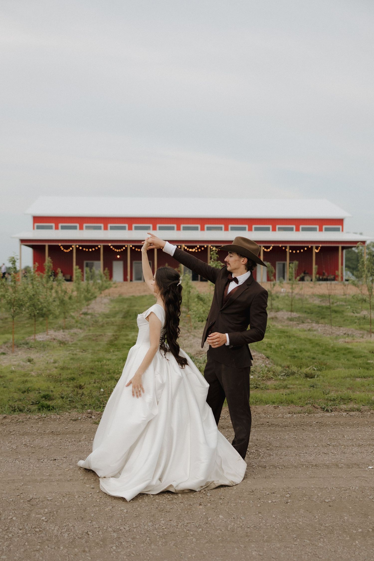 Wedding couple poses in front of a red barn structure in a rustic outdoor setting.