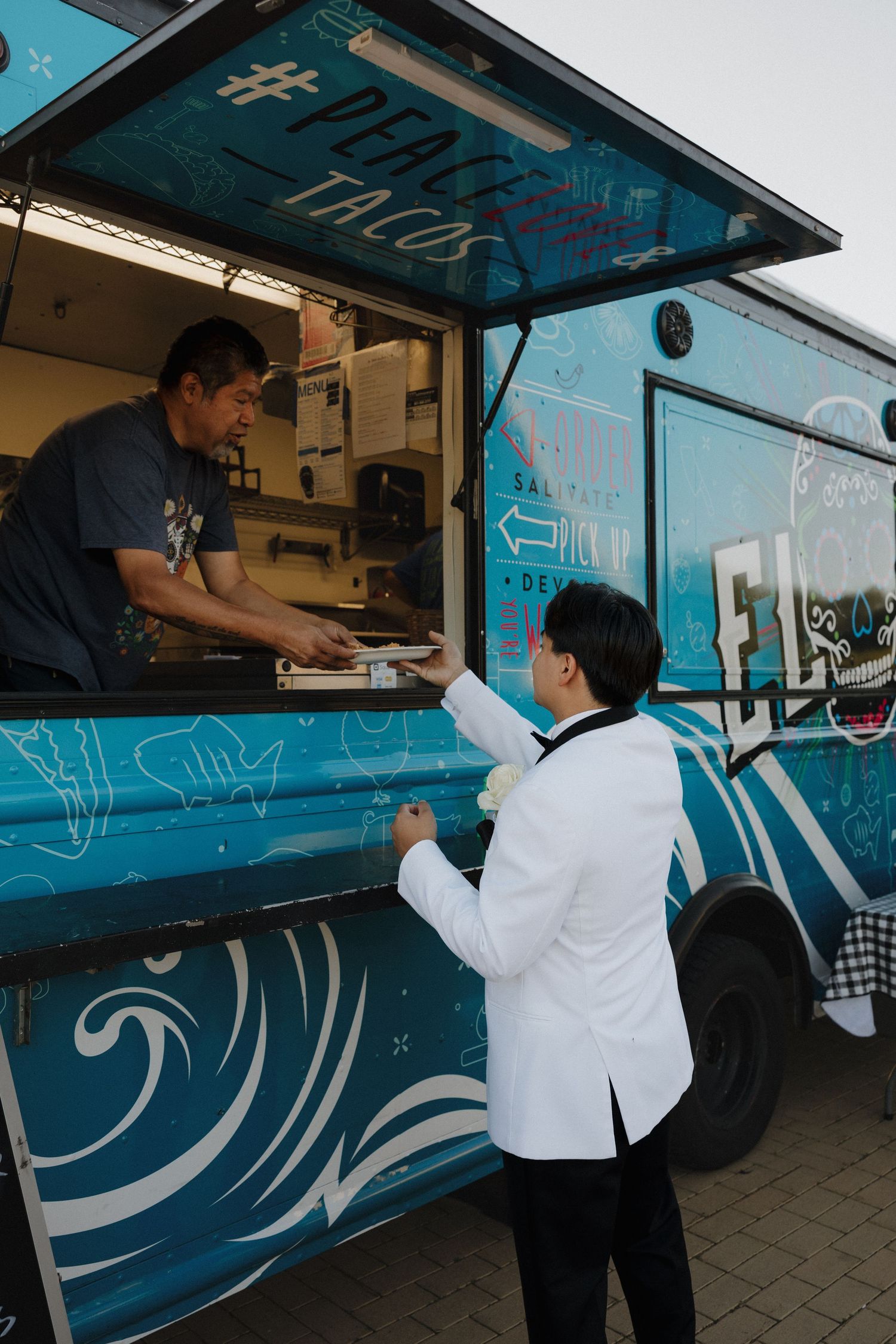 Customer ordering from a vibrant blue food truck with wave designs on its exterior.
