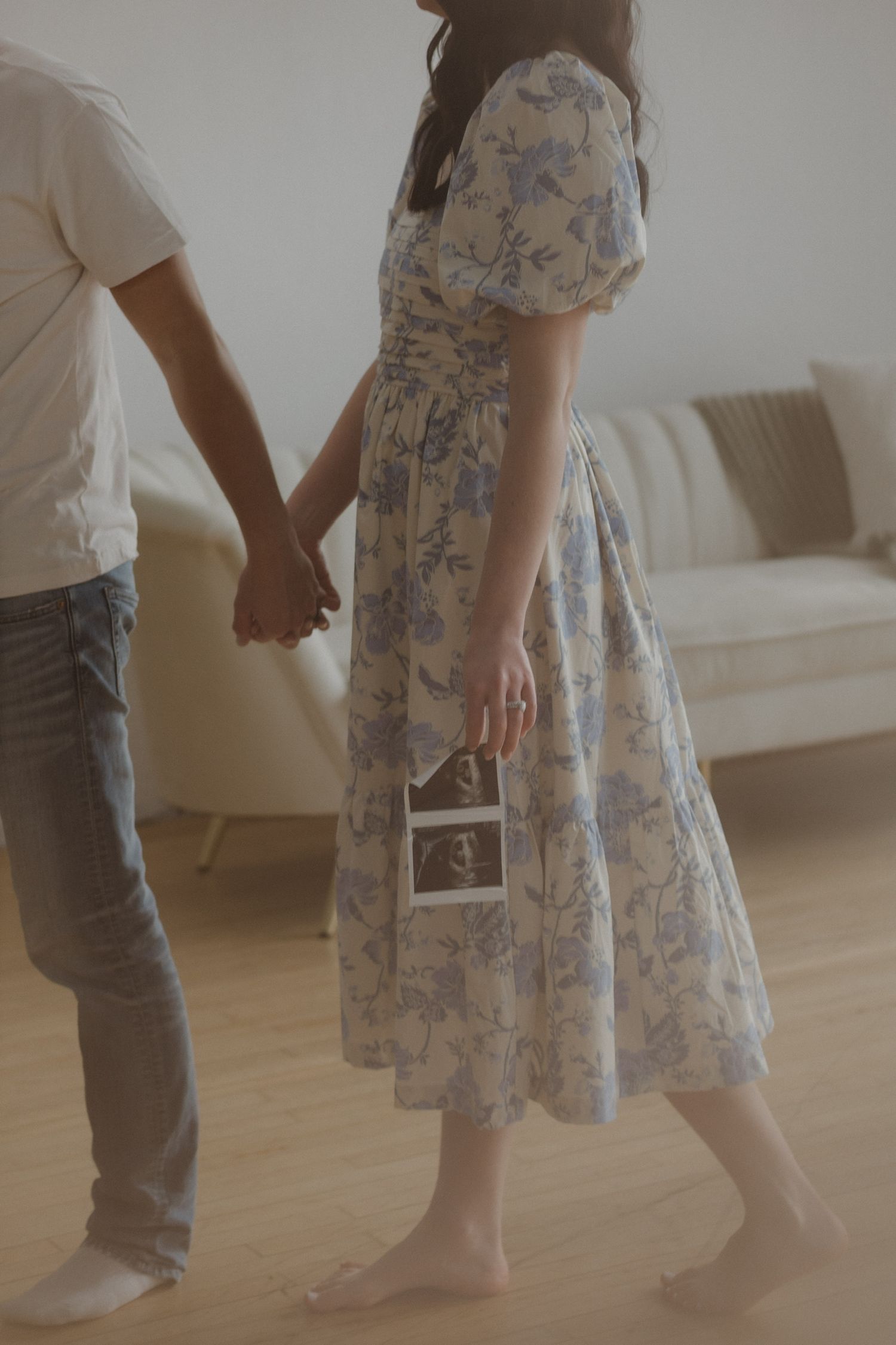 Couple holding hands while woman in floral dress holds ultrasound photos.