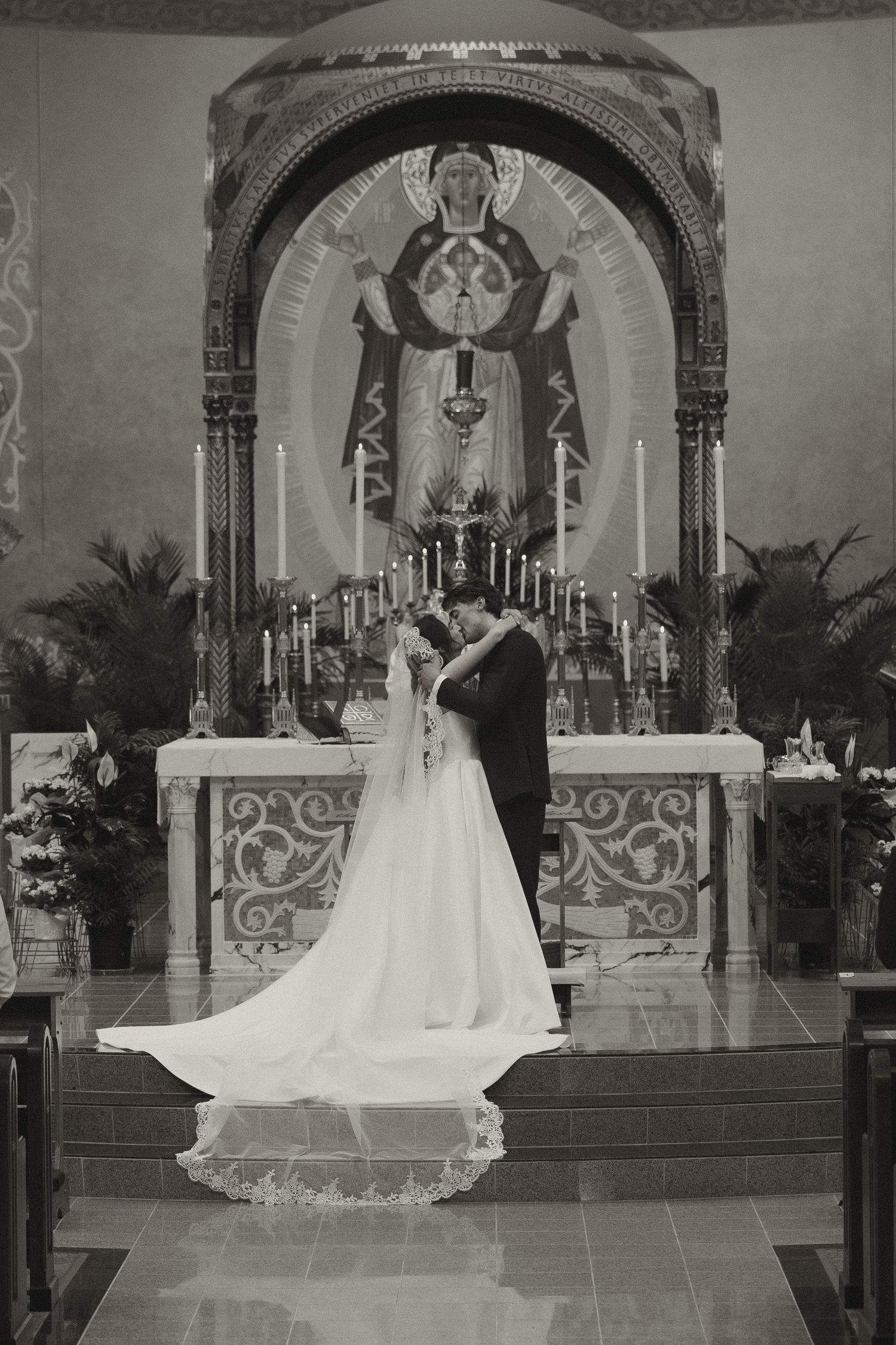 A black and white wedding ceremony photo series showing a couple at the altar of an ornate church with a long flowing veil.