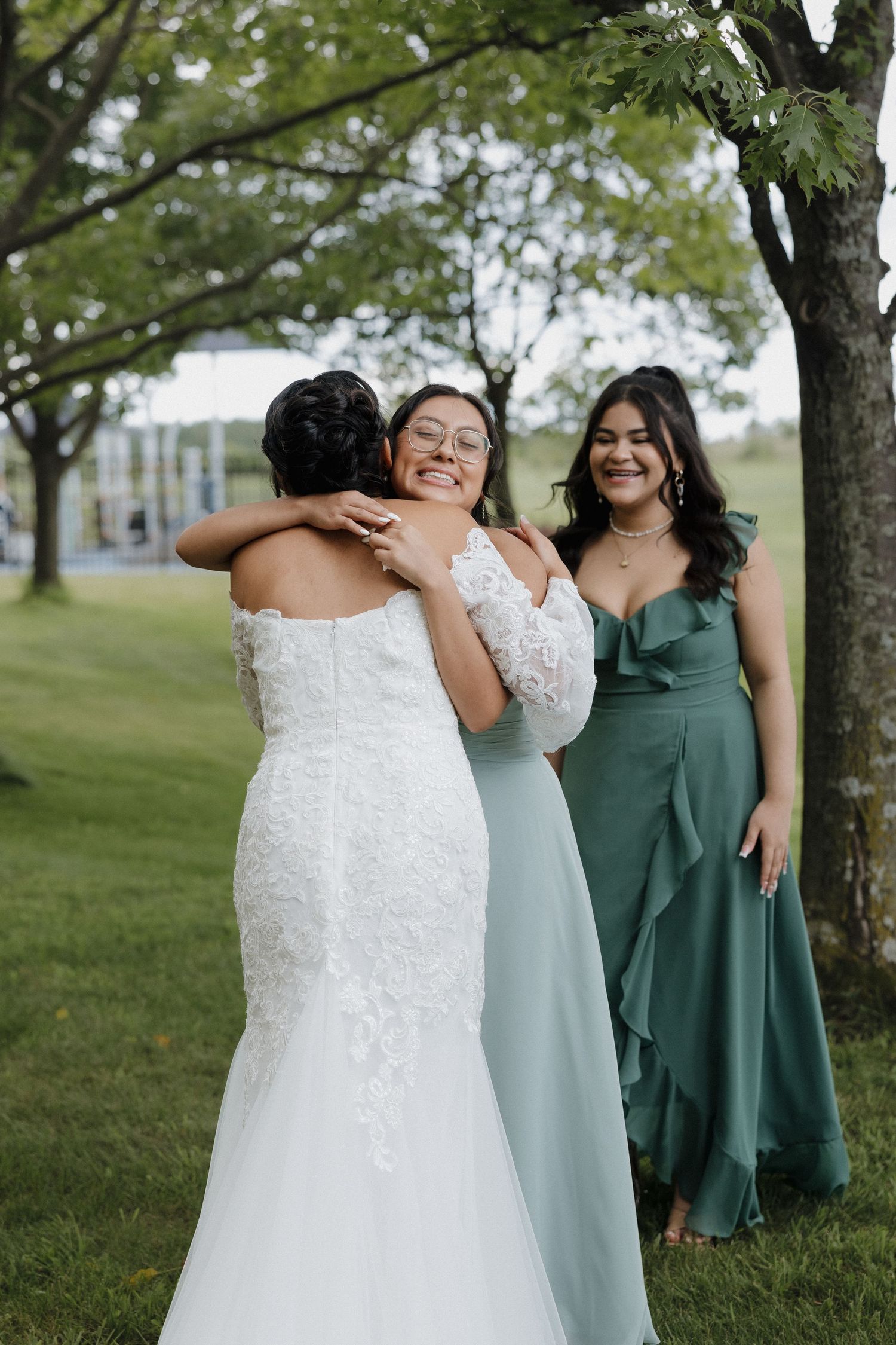 Bridesmaids in sage green dresses sharing emotional moments outdoors.