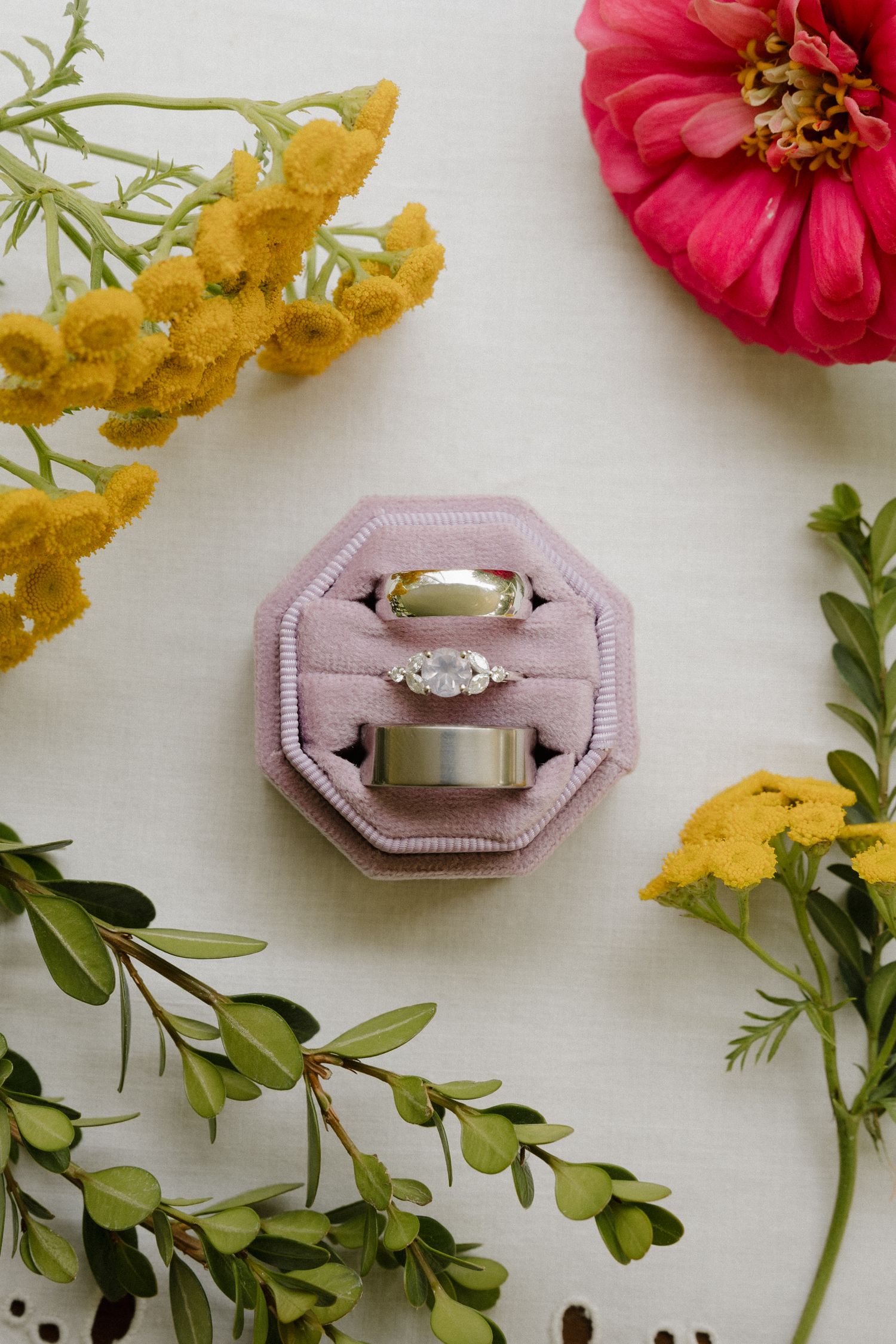 Wedding rings nestled in pink velvet boxes surrounded by red and yellow flowers on a white background.