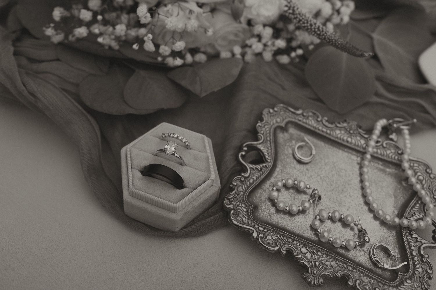 Black and white flat lay of wedding rings in velvet box with bridal jewelry accessories.