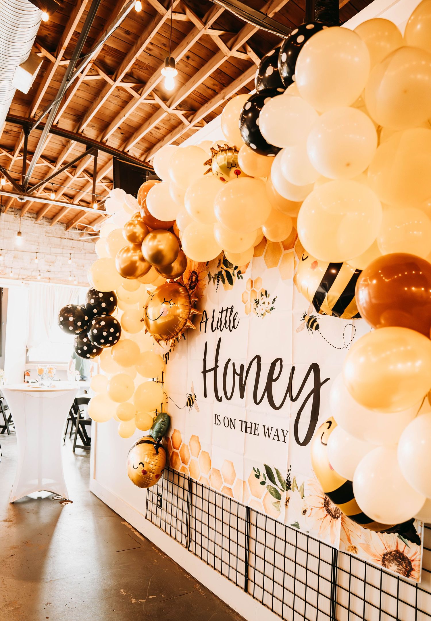 Festive balloon arch decoration with gold and white balloons against white brick wall.