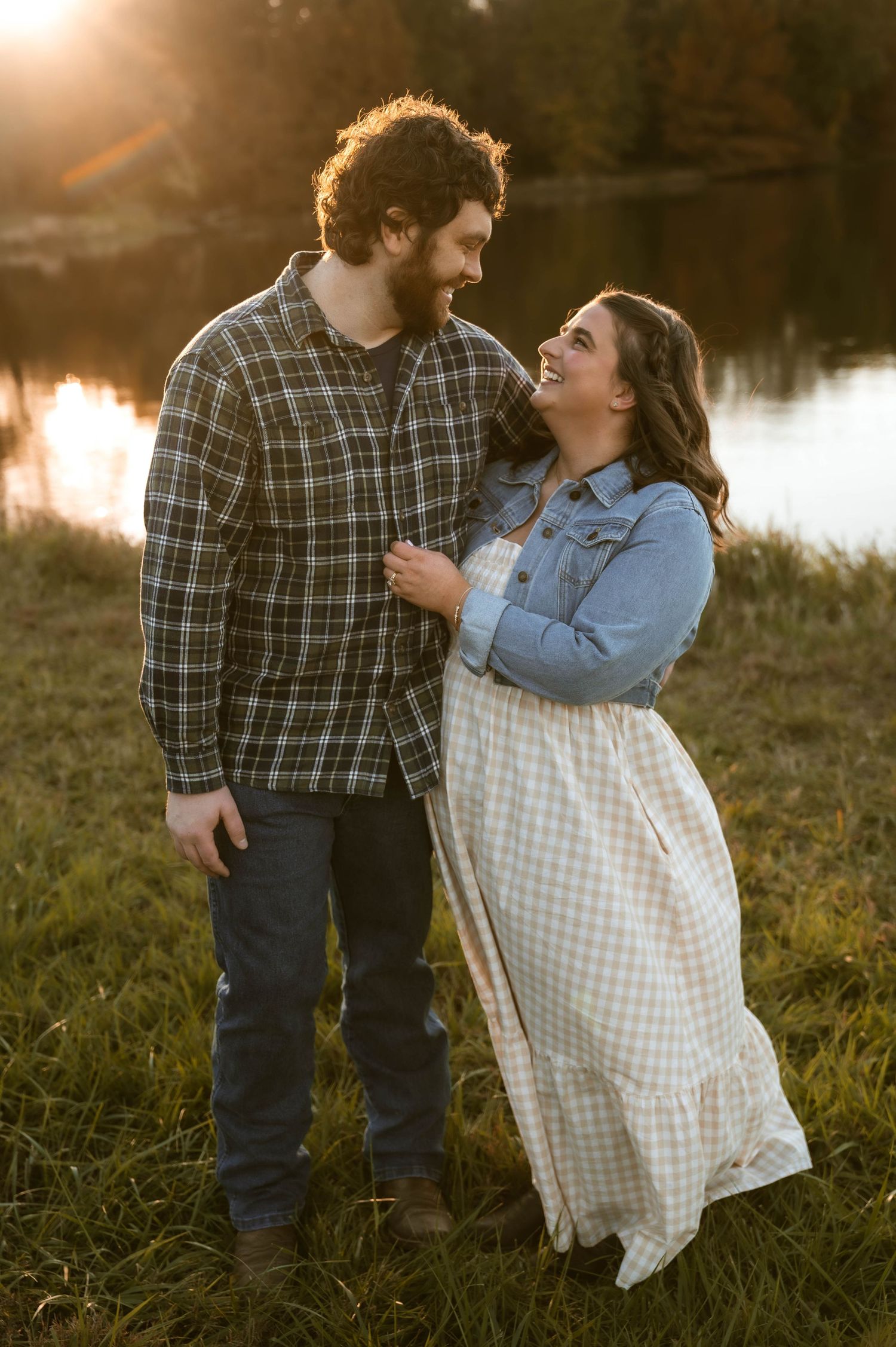 Happy couple laughing together by a lake at sunset.