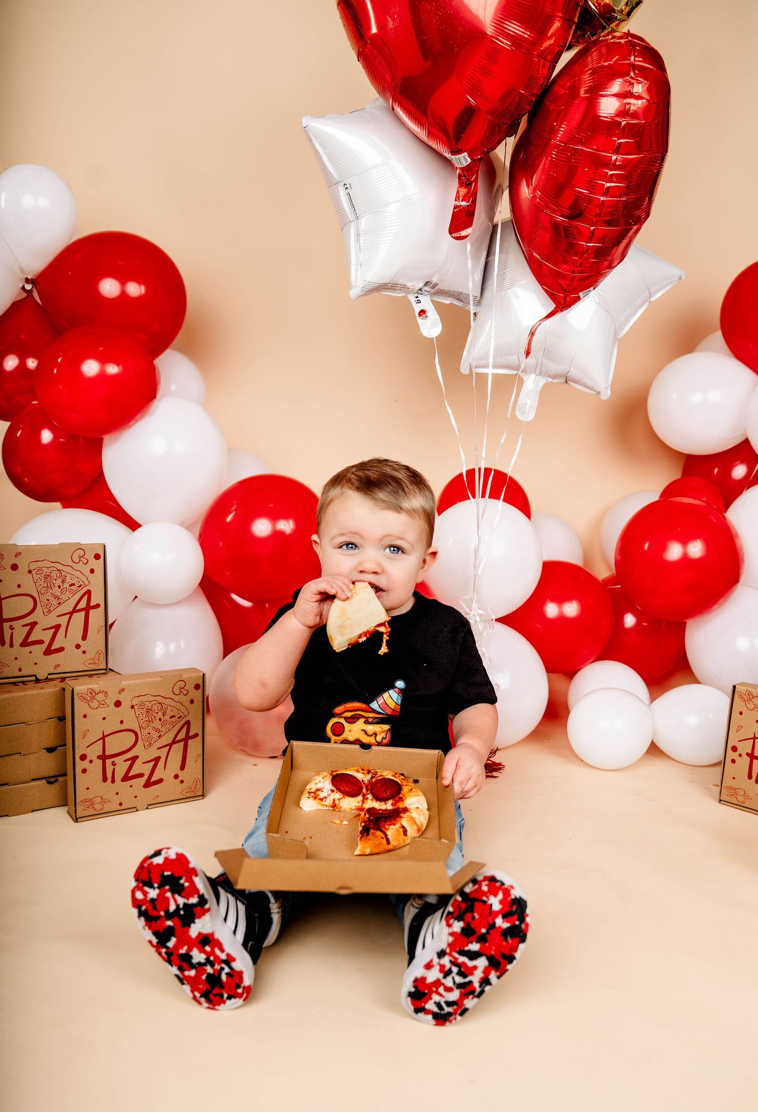 Child sits among red and white balloon decorations during a celebration.