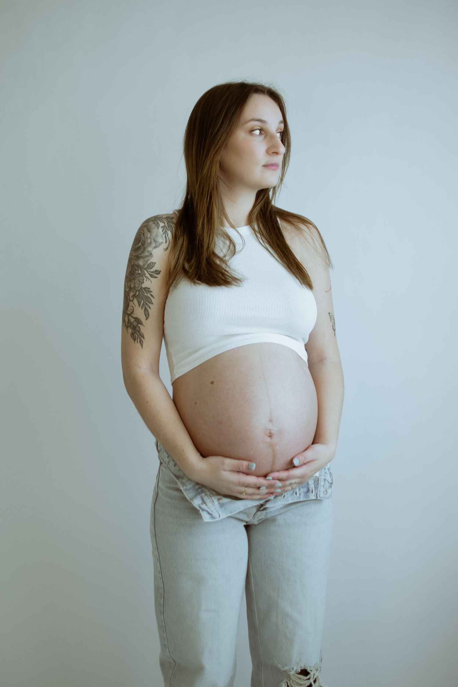 Side view maternity portraits showing pregnant woman in casual attire against neutral backdrop.