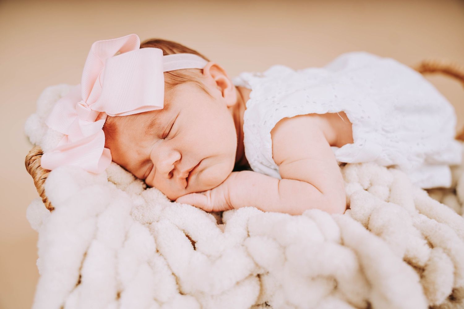 Peaceful sleeping baby wearing pink bow on cozy white blanket.