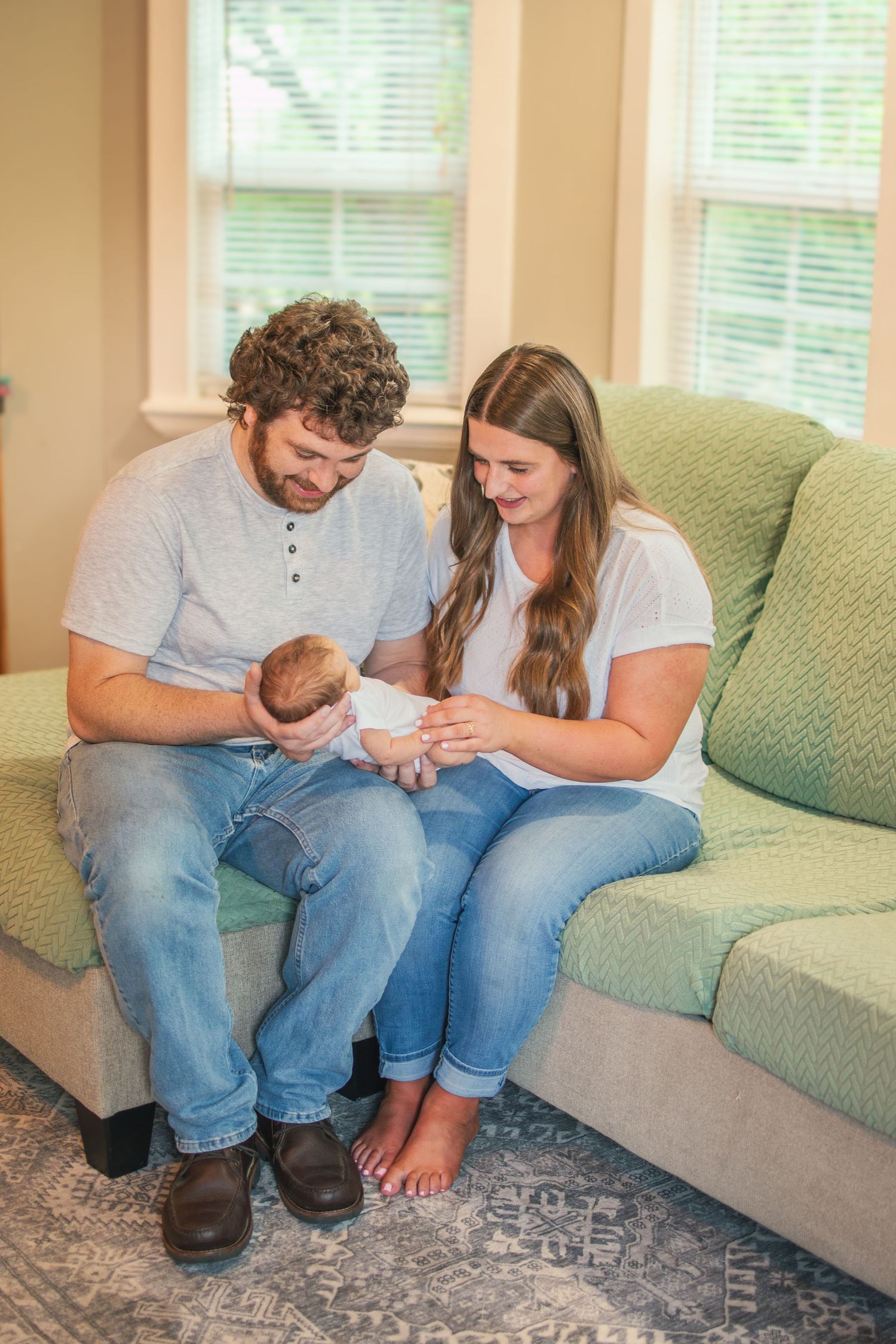 Couple sitting on green couch while holding their newborn baby.