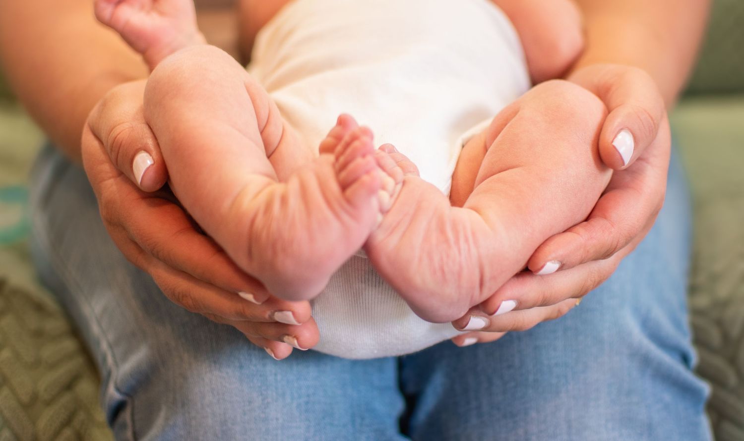 Gentle hands cradling tiny newborn feet against soft fabric.