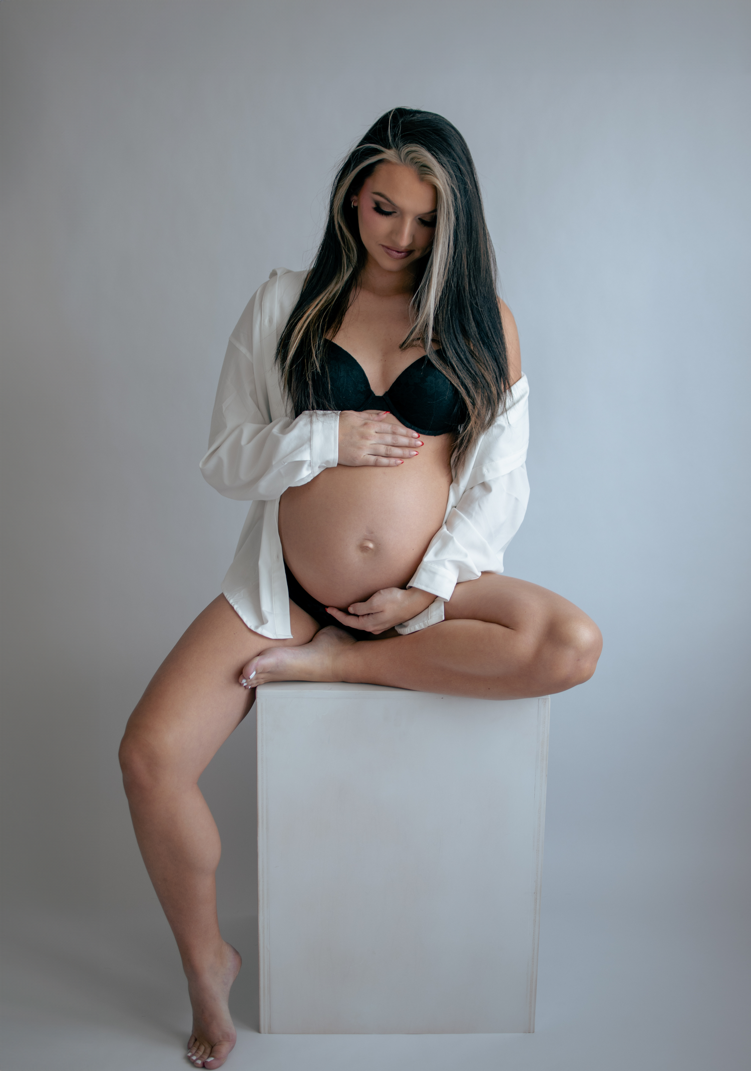 Minimalist maternity photography with white shirt and artistic composition against neutral background.