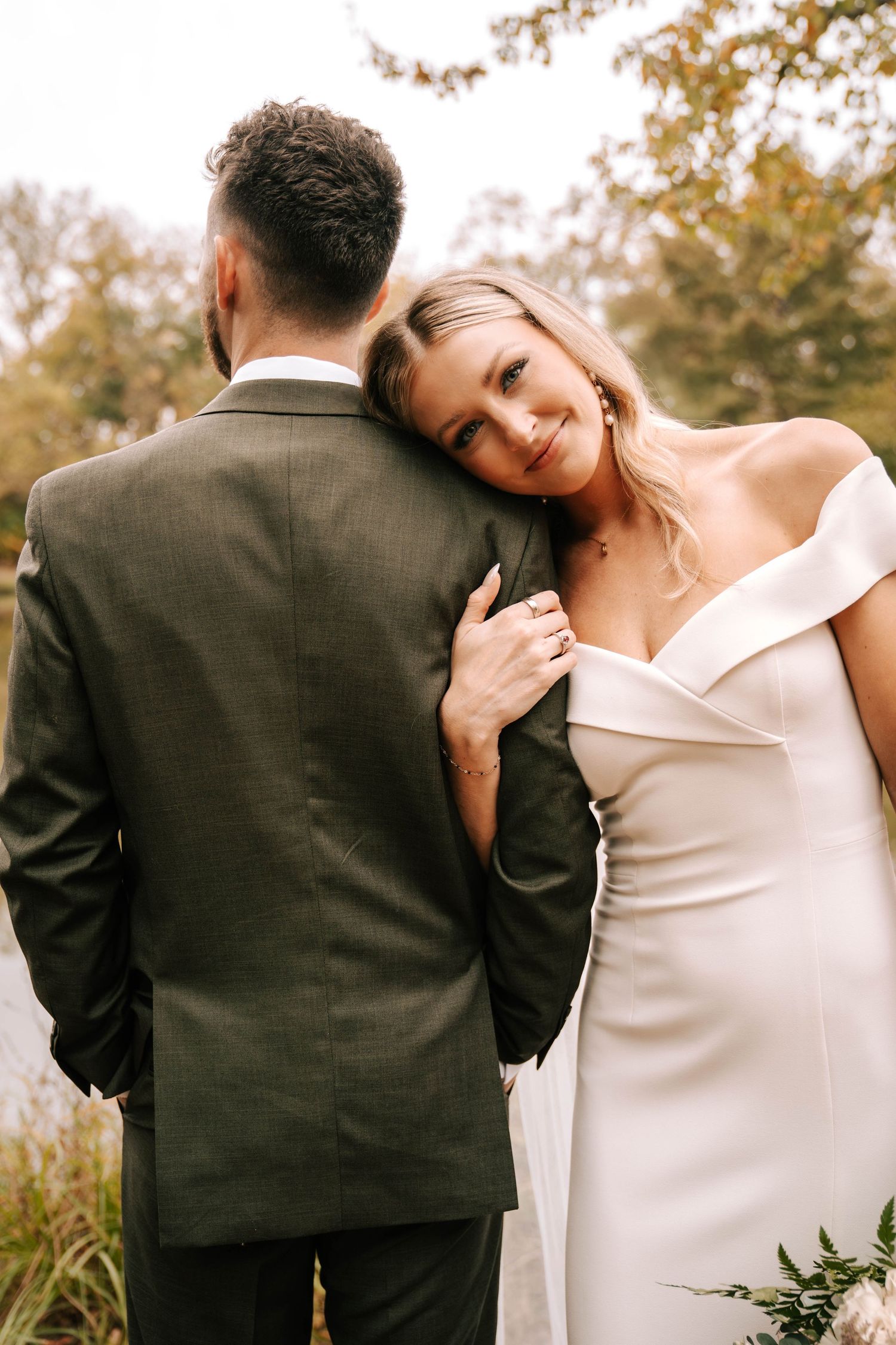 Romantic wedding couple embraces in an outdoor autumn setting wearing elegant white dress and dark suit.