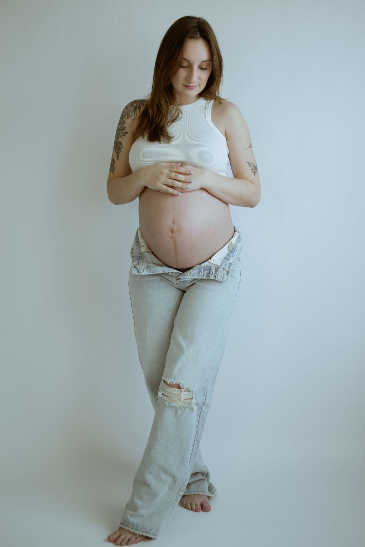 Casual maternity photos showing pregnant woman in distressed jeans and white top.