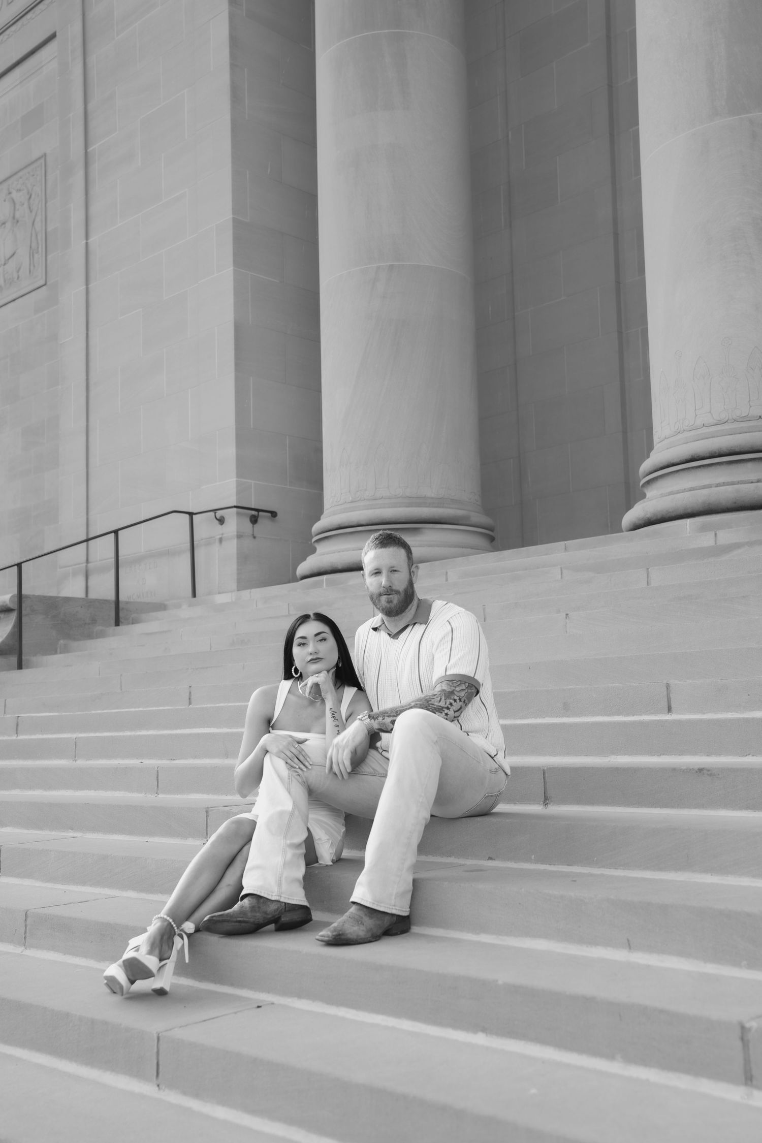 Black and white photo of a couple sitting on grand stone steps with tall columns behind them.