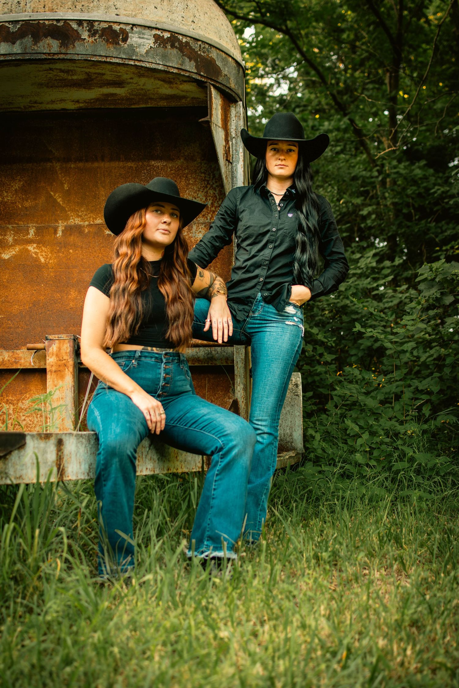Couple in western attire sitting together on rustic wooden steps surrounded by greenery.