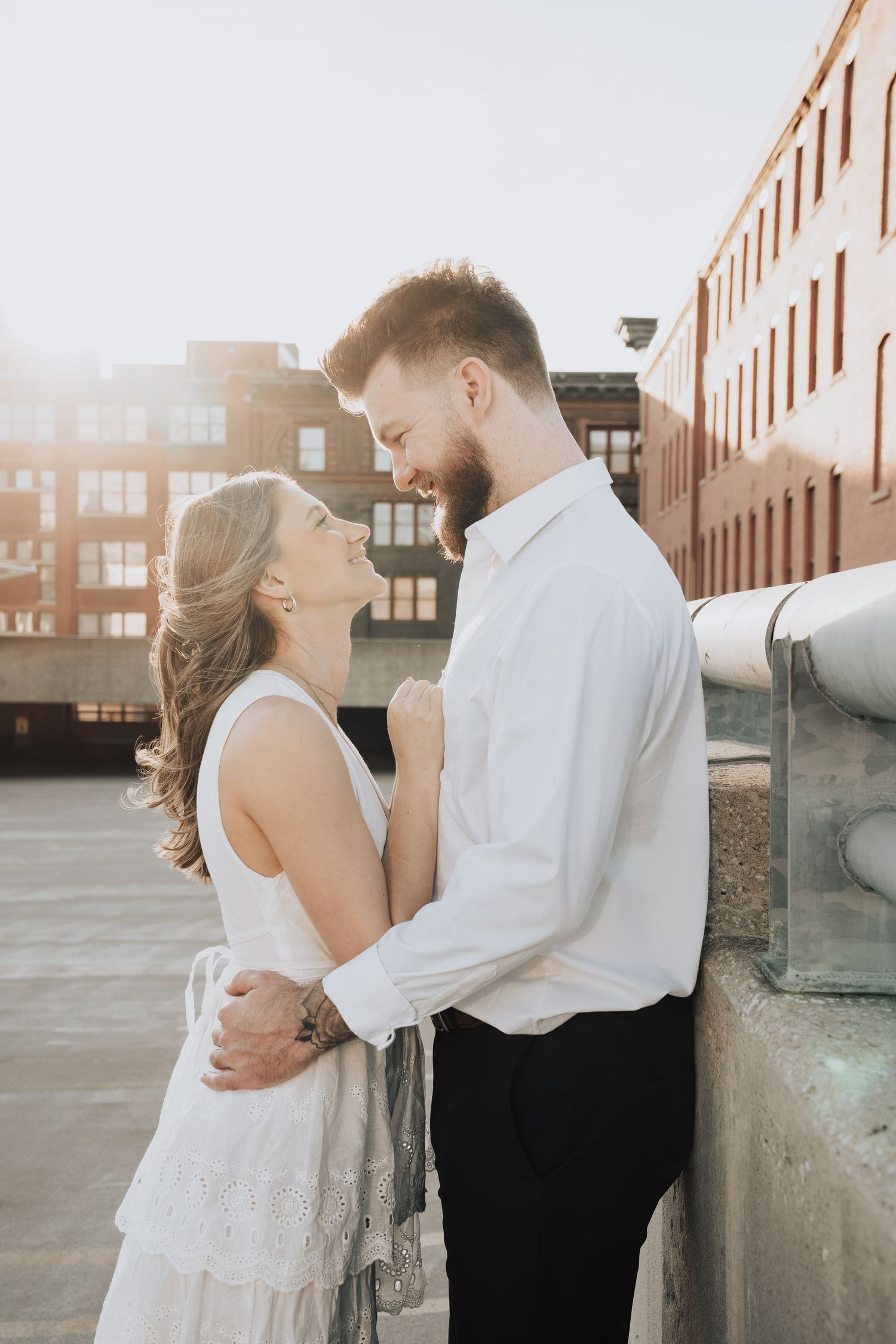 A romantic couple embraces on a rooftop at sunset with brick buildings in the background.
