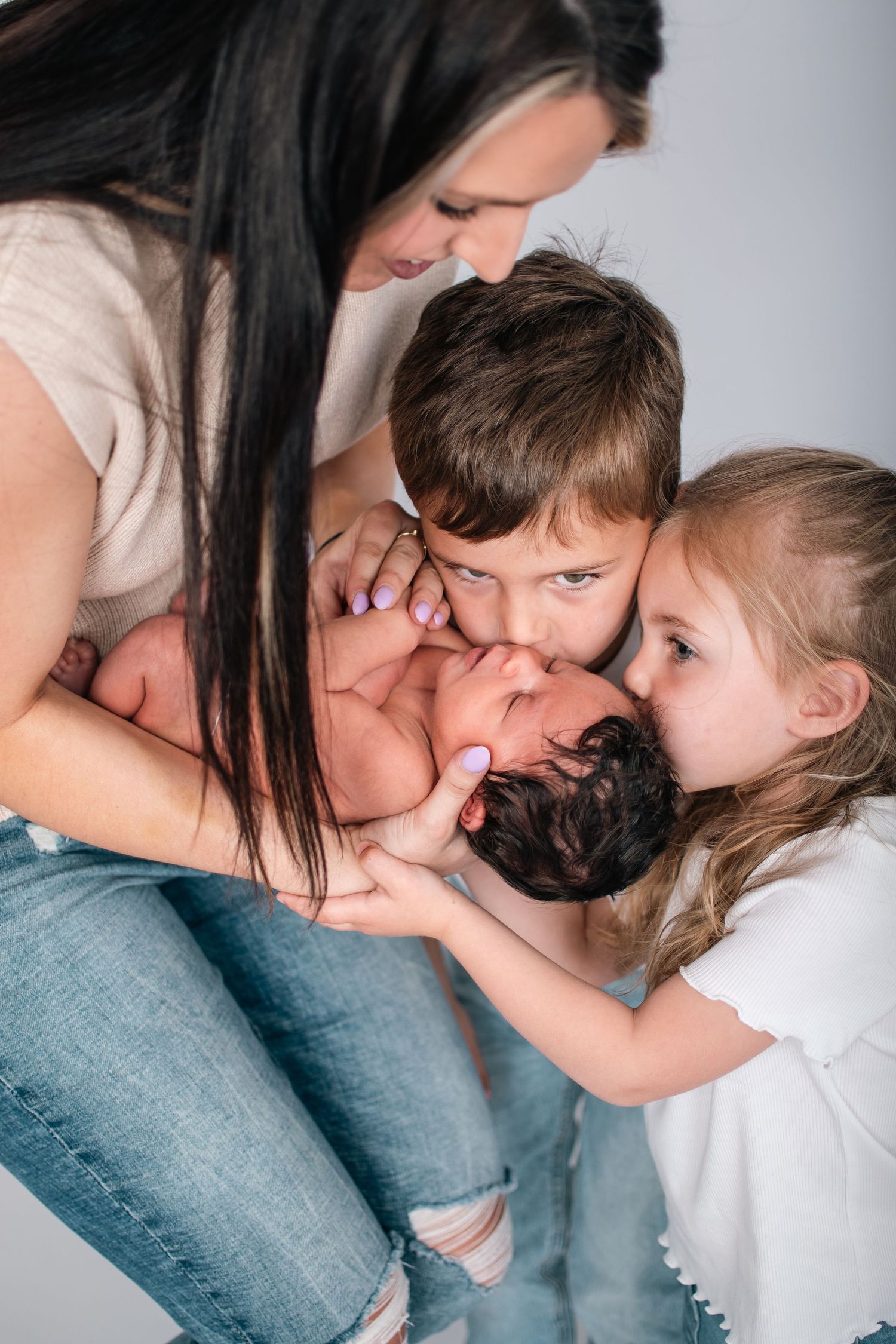Family gathered close together sharing intimate moment with newborn baby in studio setting.