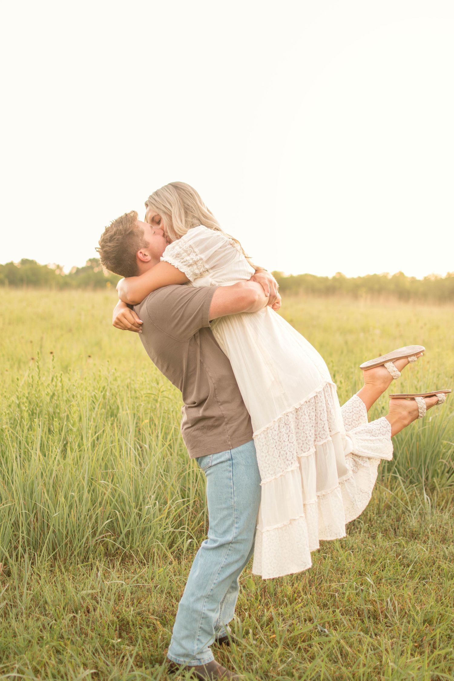 Playful couple dancing and twirling in a grassy field at dusk.
