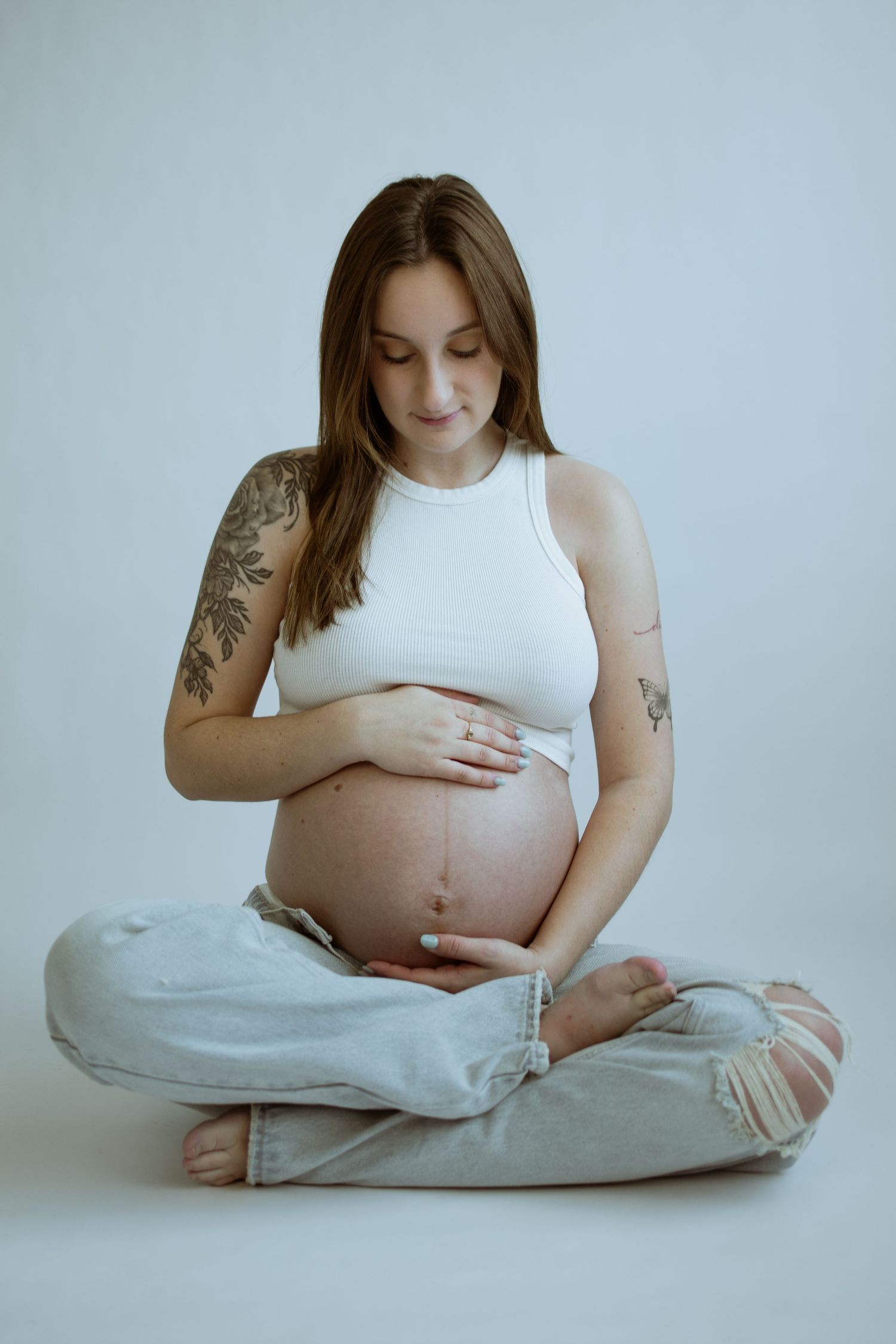 Serene maternity photos showing woman cradling baby bump while sitting on floor.