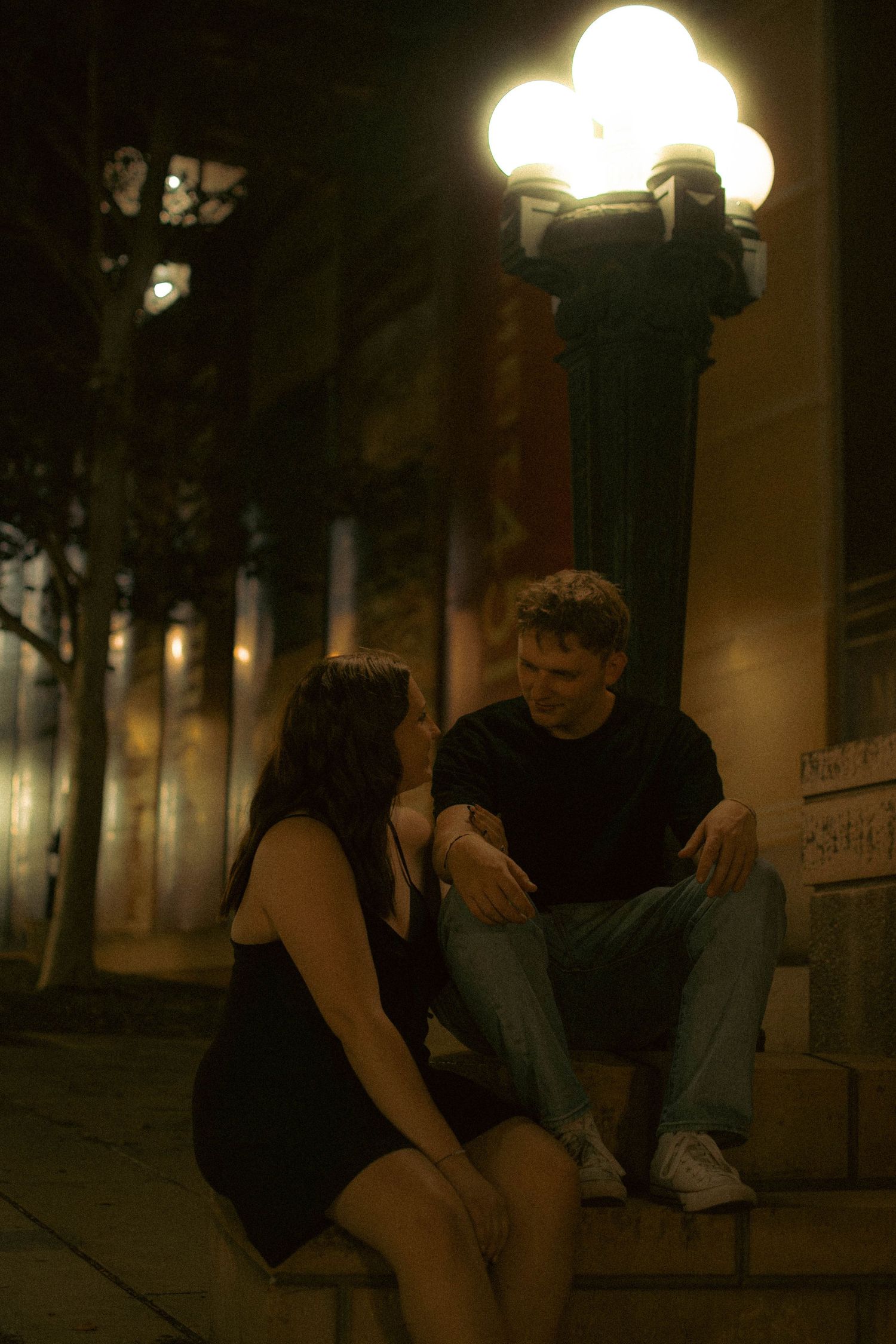 Couple sitting together under street lamps at night.