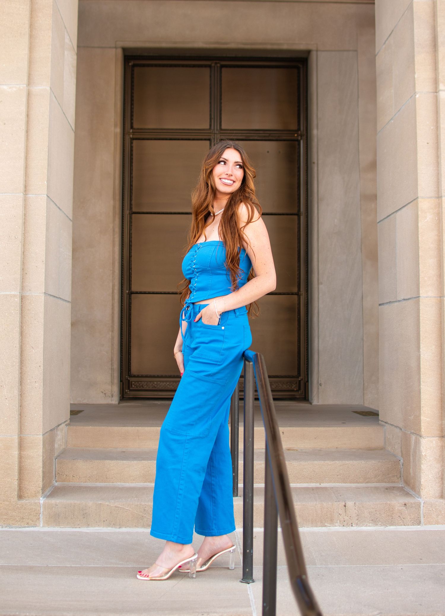 Woman in bright blue dress poses on stone building steps.