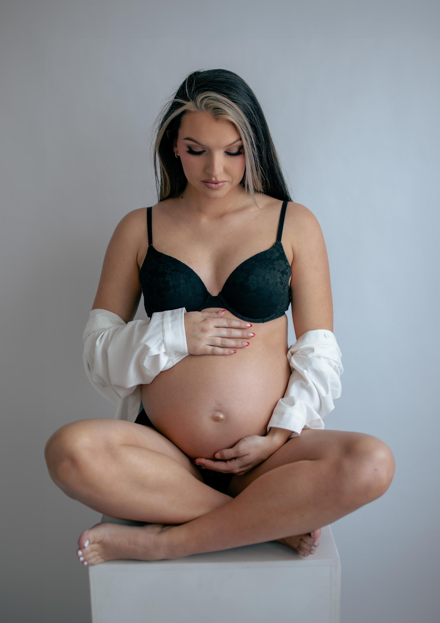 Intimate maternity portrait with black bra and white sleeves in studio setting.