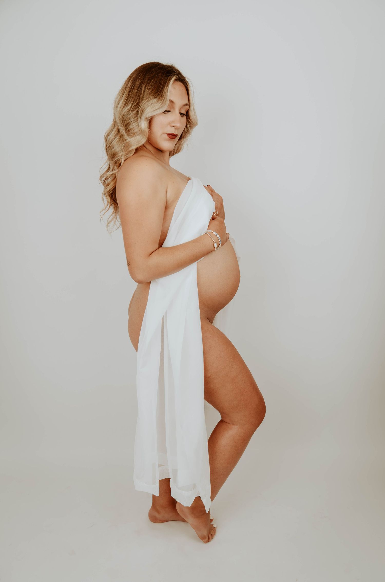 An artistic maternity photo with flowing white fabric against a light backdrop.