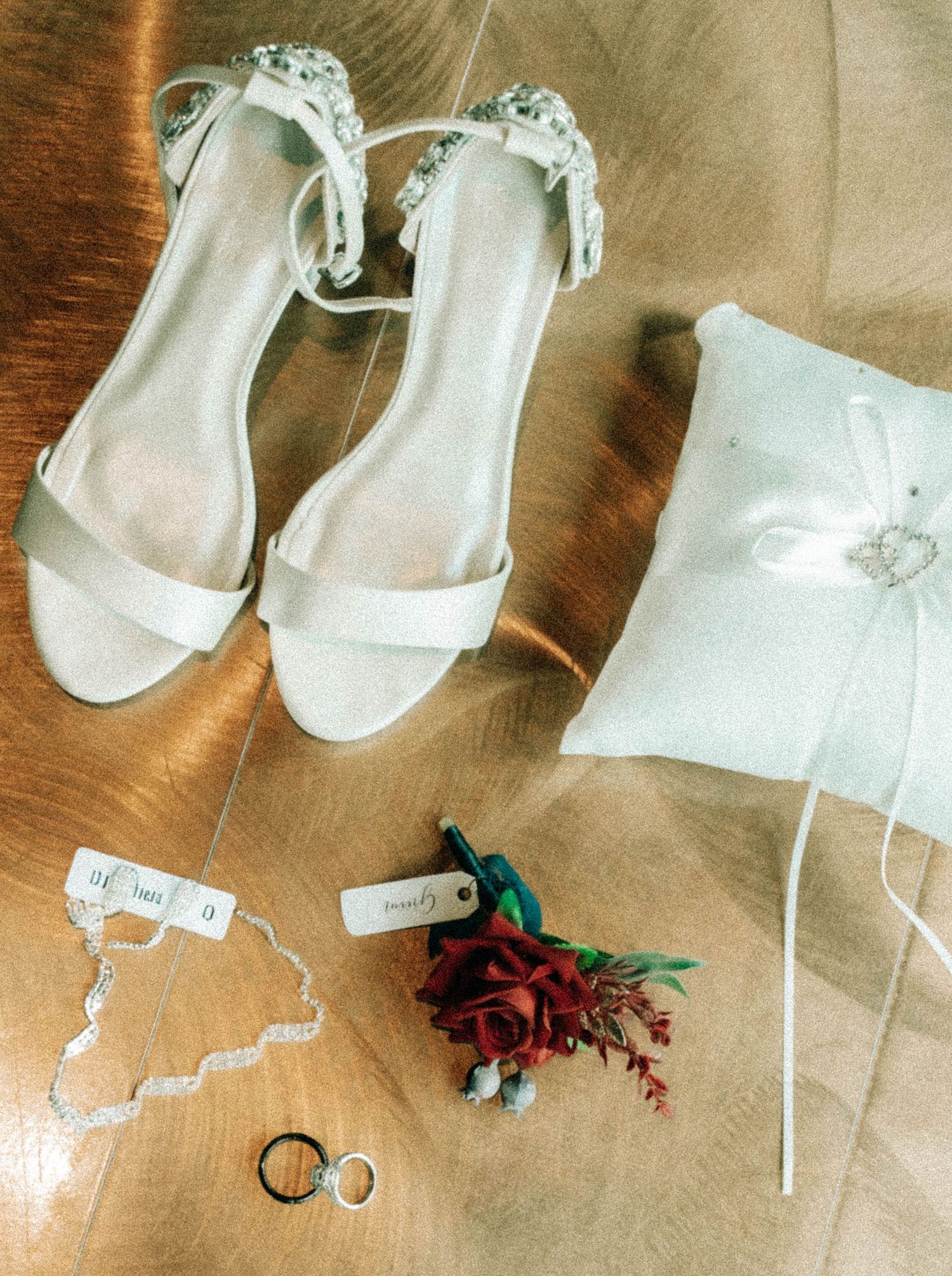 White bridal shoes and wedding accessories arranged on wooden surface.