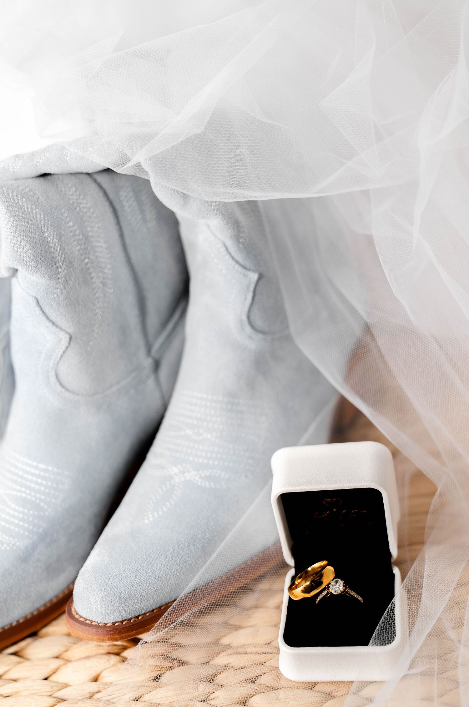 White cowboy boots with wedding ring boxes displayed against tulle fabric.