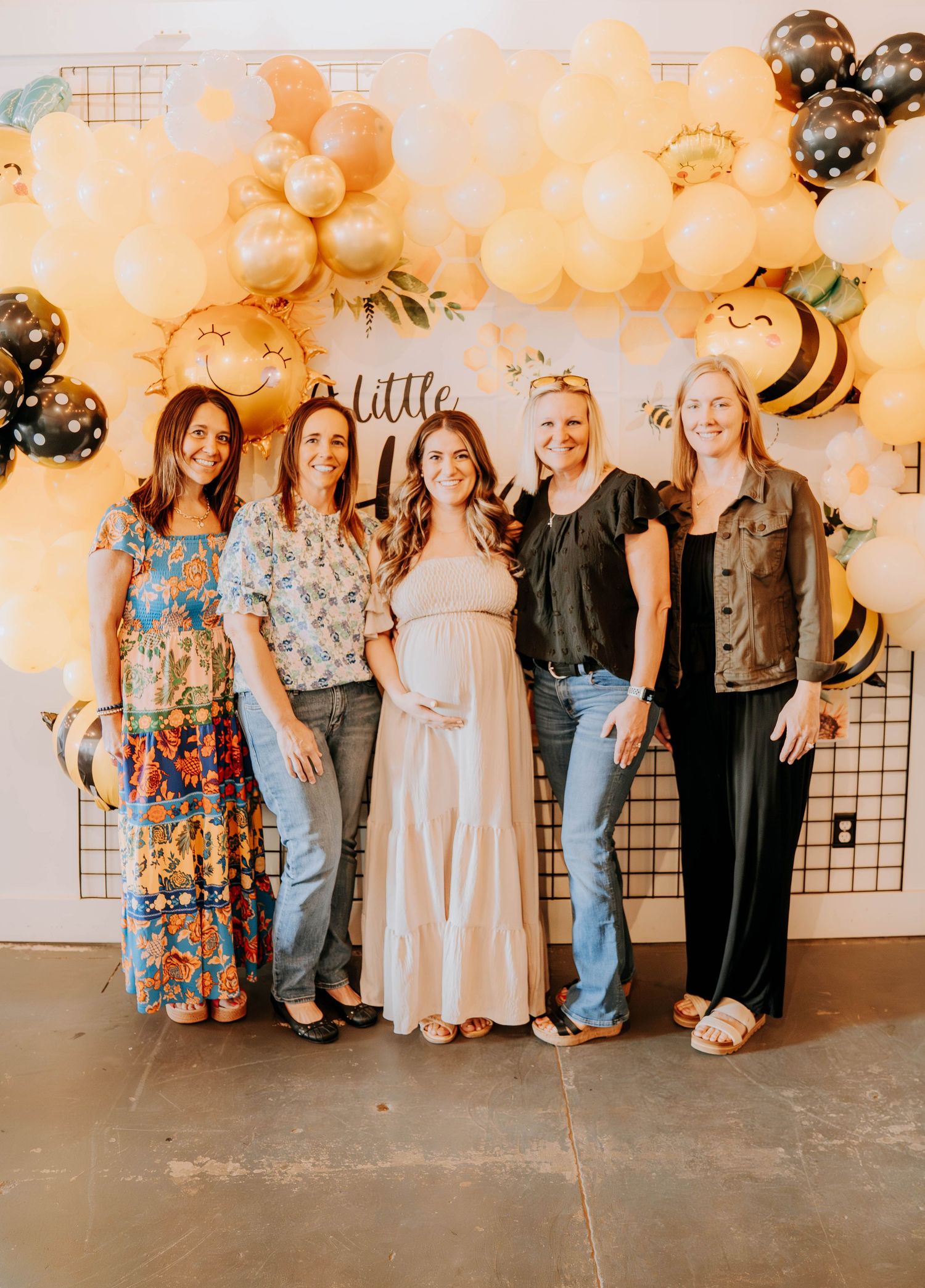 Group photo against peach-colored balloon wall backdrop with decorative bee elements.