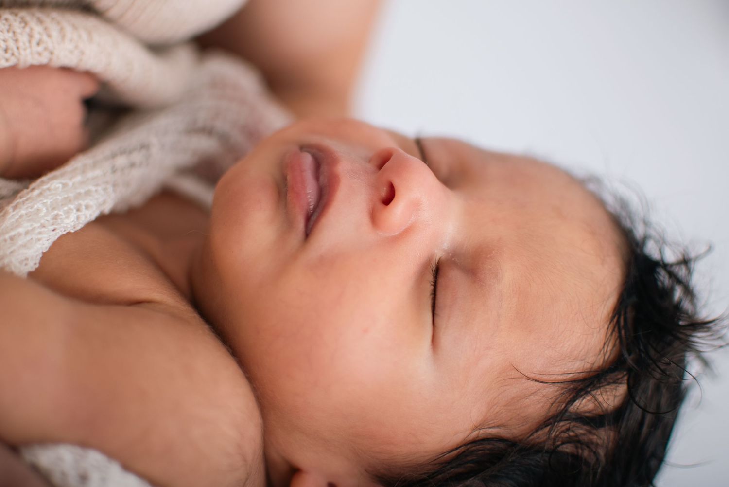 Close-up of peaceful sleeping newborn baby wrapped in knit blanket.