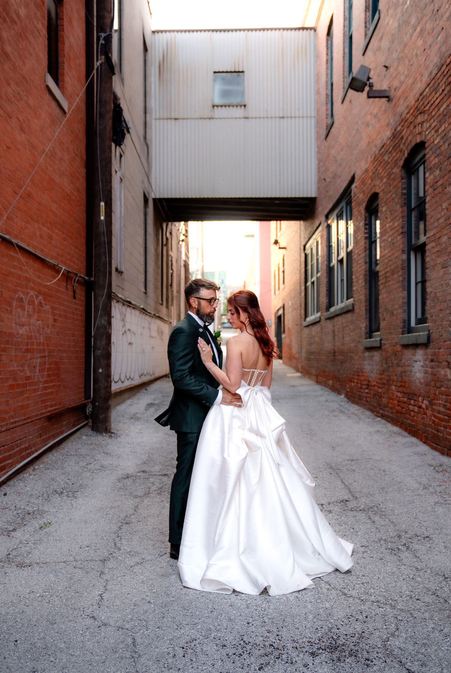 Bride and groom share a romantic moment in a rustic brick alley, bride in elegant white ballgown.