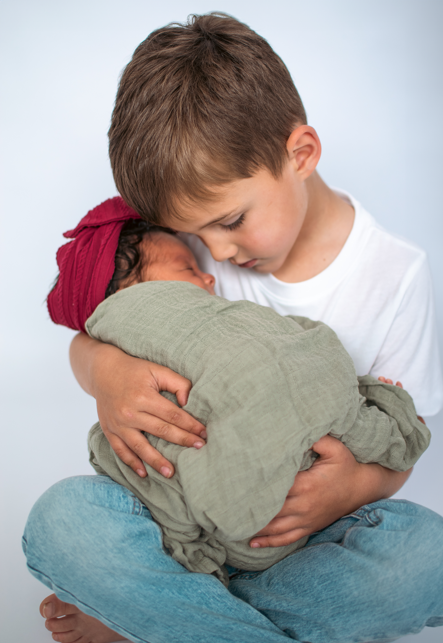 Young child tenderly holding and looking down at a swaddled infant.