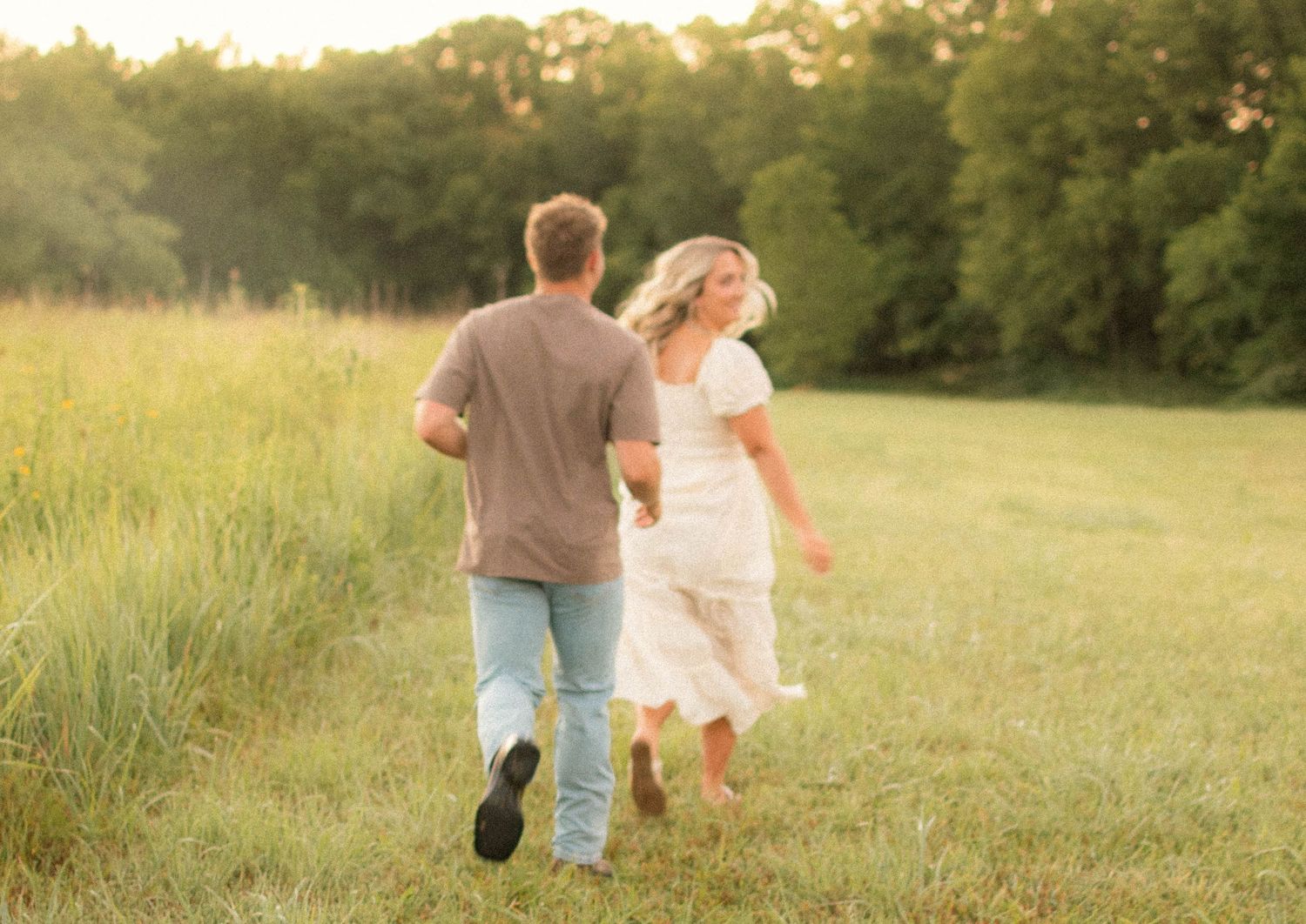 Couple walking hand in hand through a sunlit meadow.