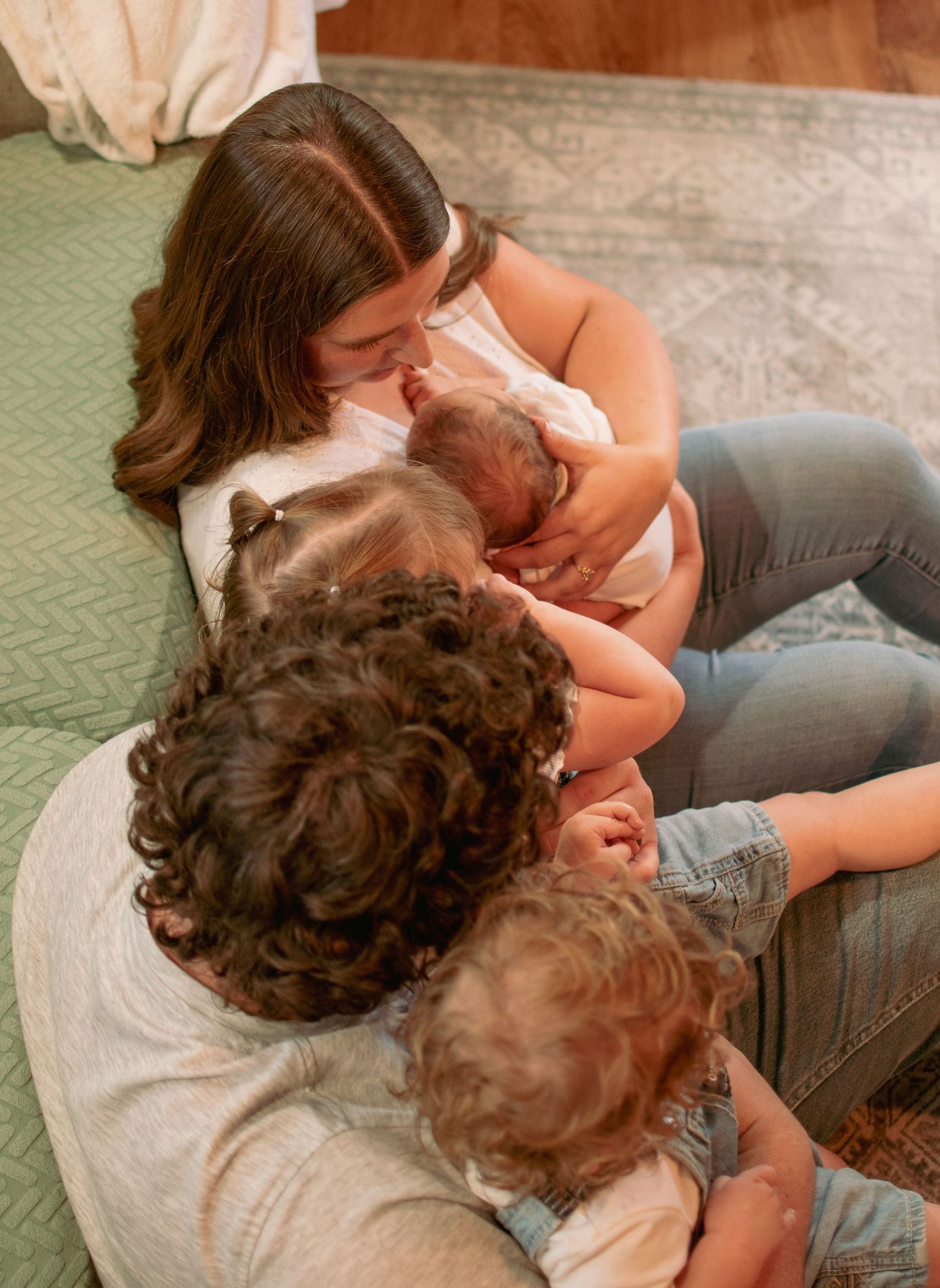 Family cuddling together on floor with newborn in intimate moment.