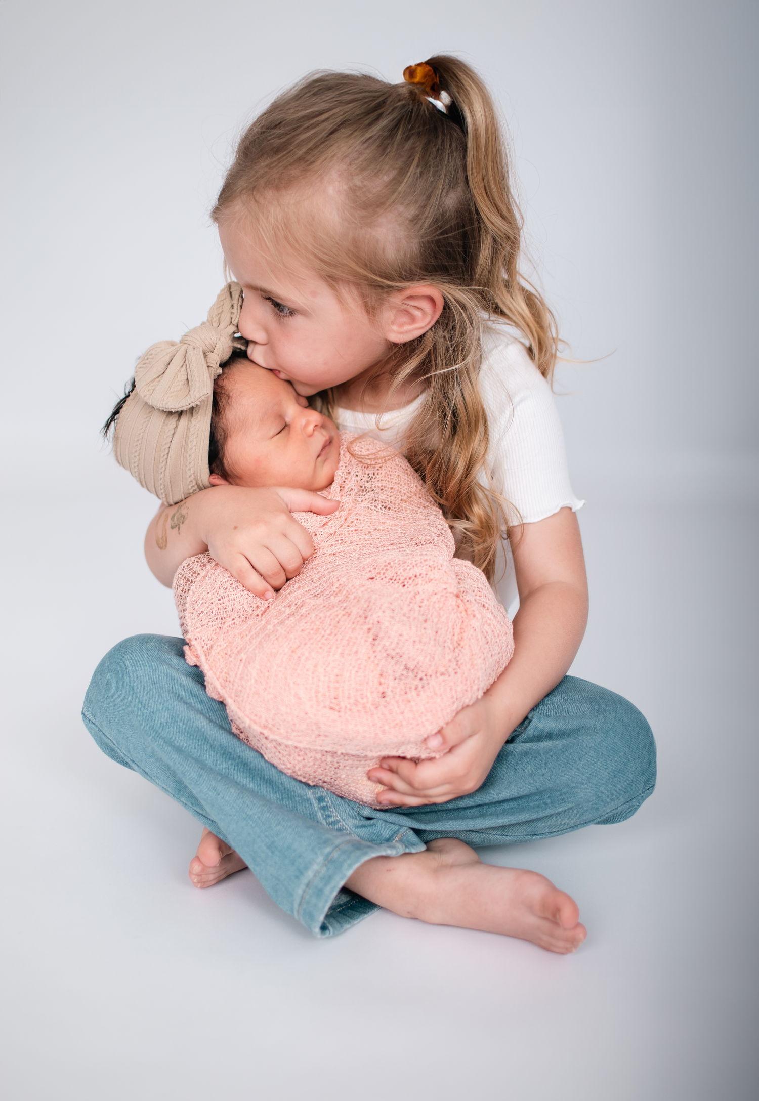 Sweet moment of young girl in white shirt and jeans holding newborn baby wrapped in pink.