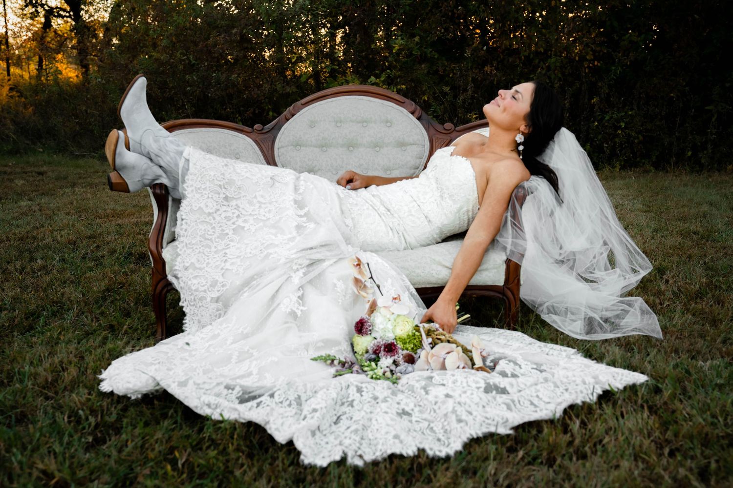 Bride in lace wedding dress poses gracefully on grass during sunset photo session.