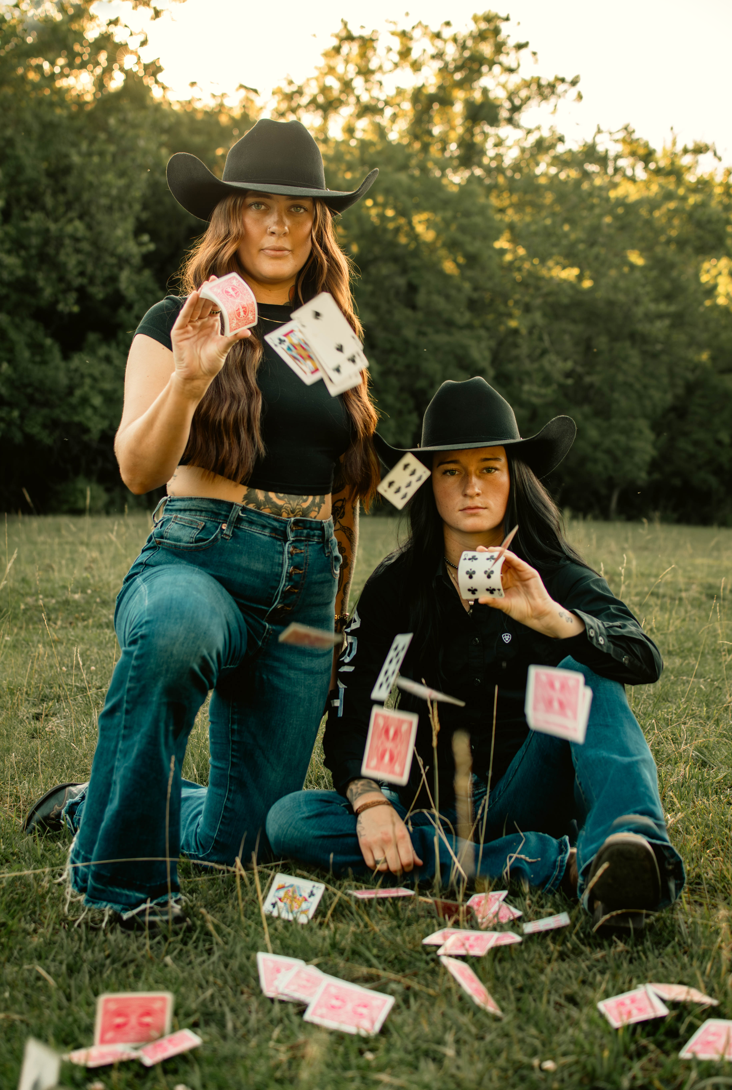 Couple playing cards on grass with scattered playing cards around them.