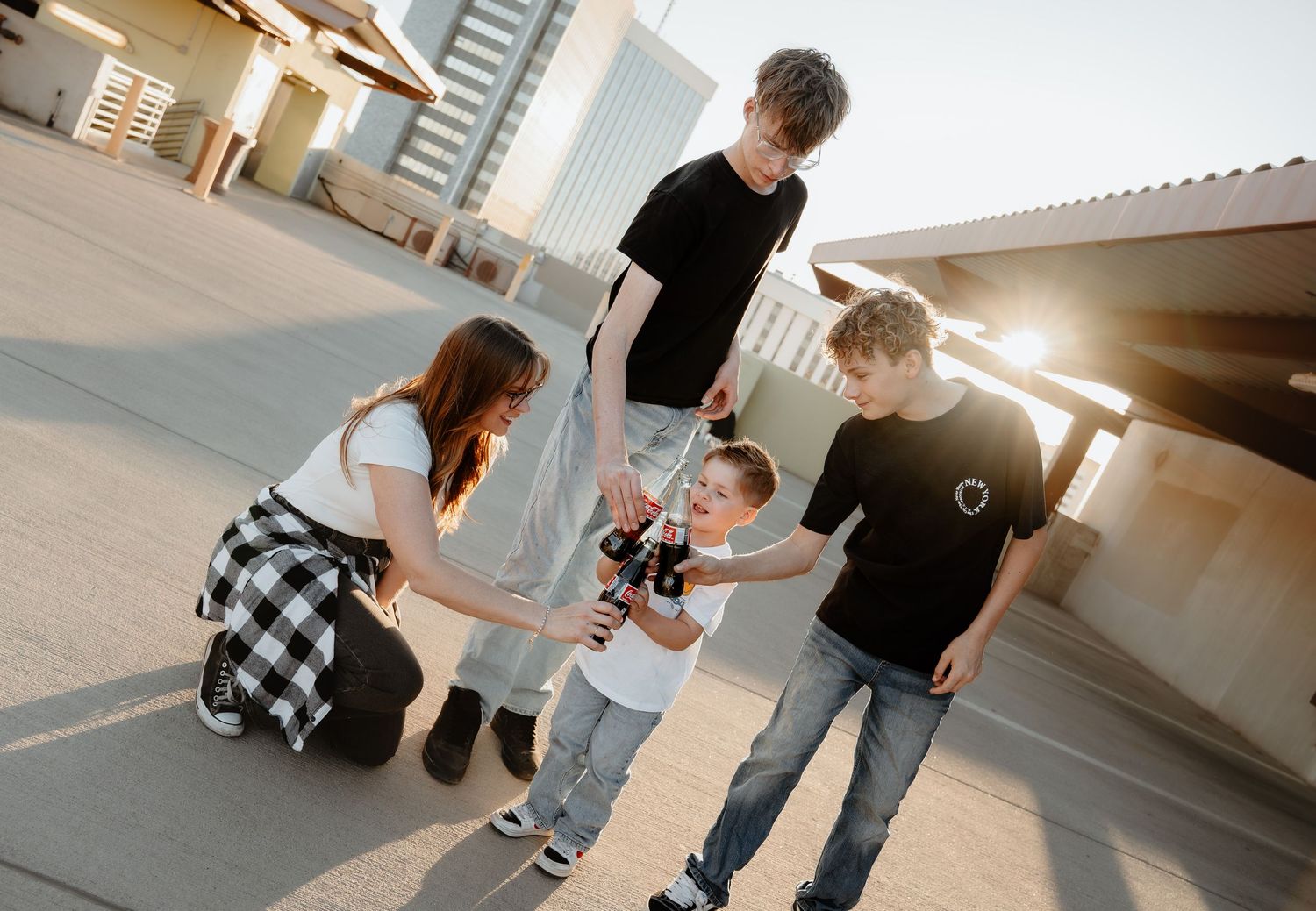 Group of kids and a woman kneeling outdoors on a rooftop, sharing a moment in warm sunlight.
