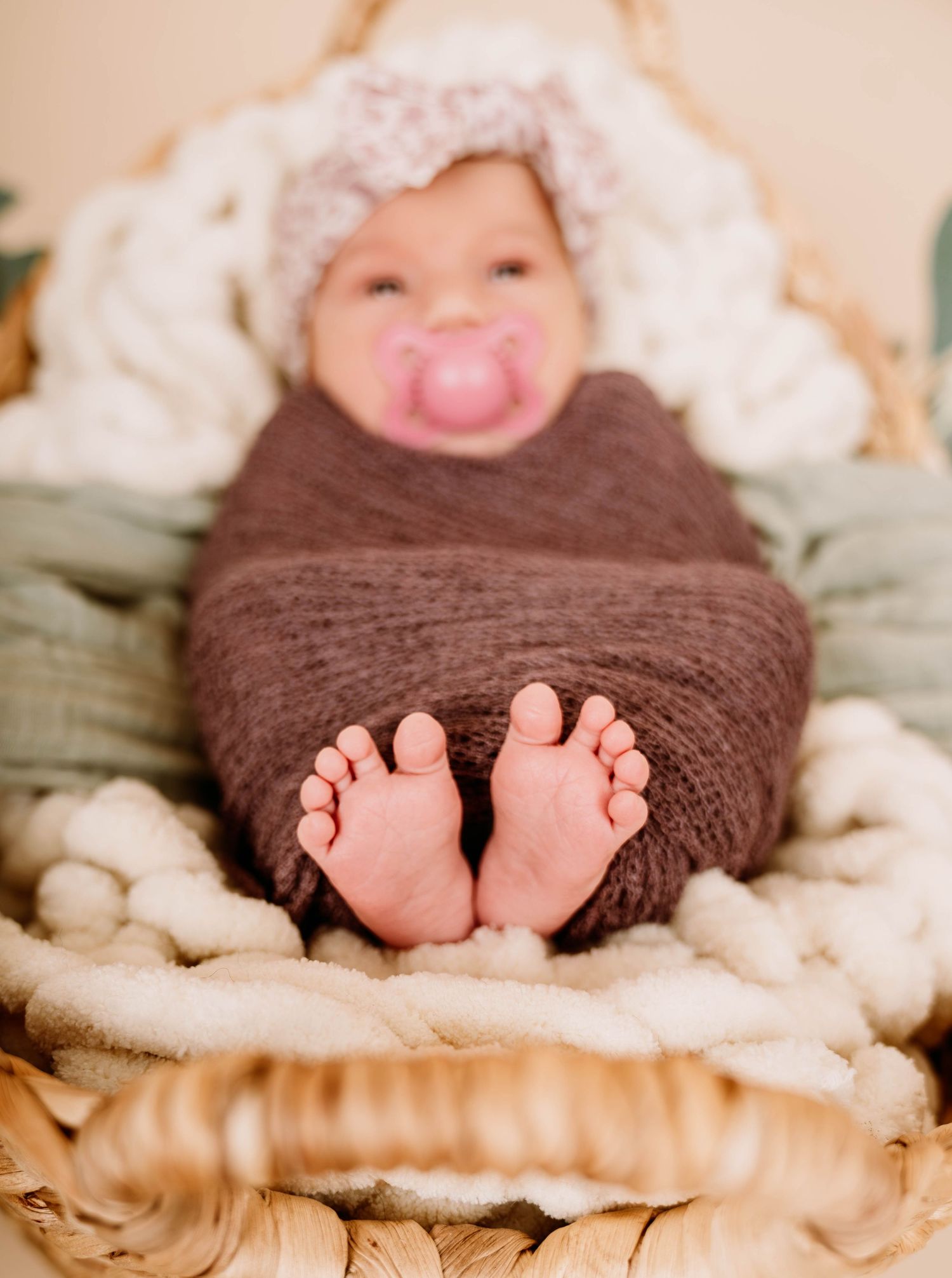 Baby wearing brown knit wrap with tiny feet showing against cream colored blanket.