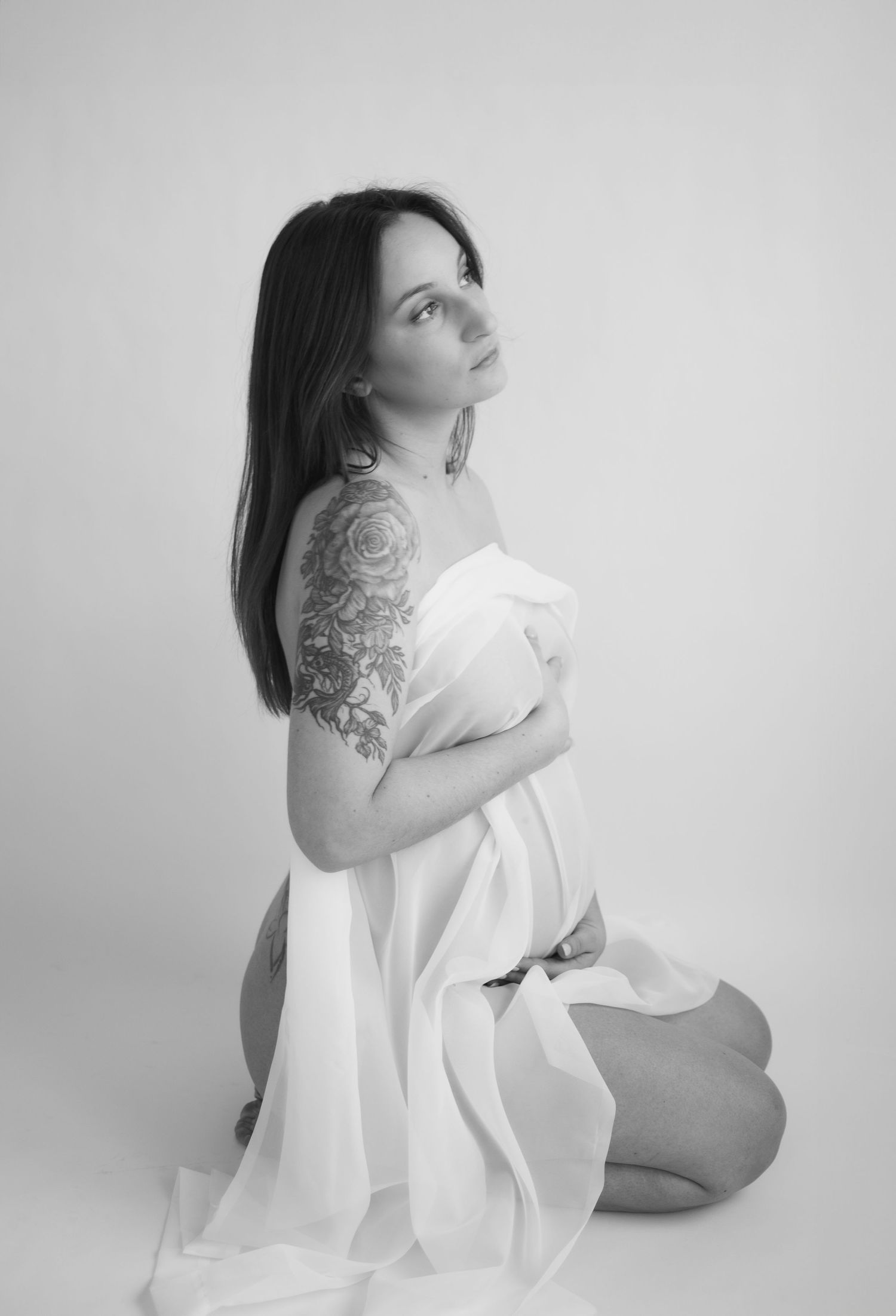 Artistic maternity portraits in flowing white fabric against light background.