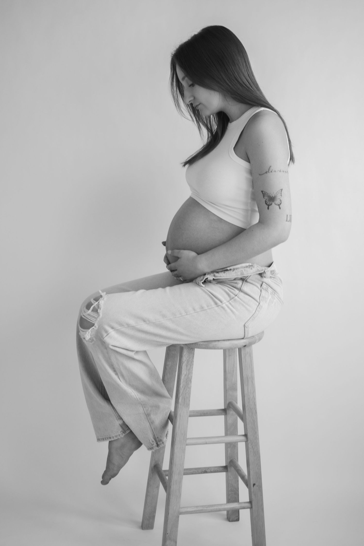 Artistic black and white maternity photos of woman sitting on wooden stool.