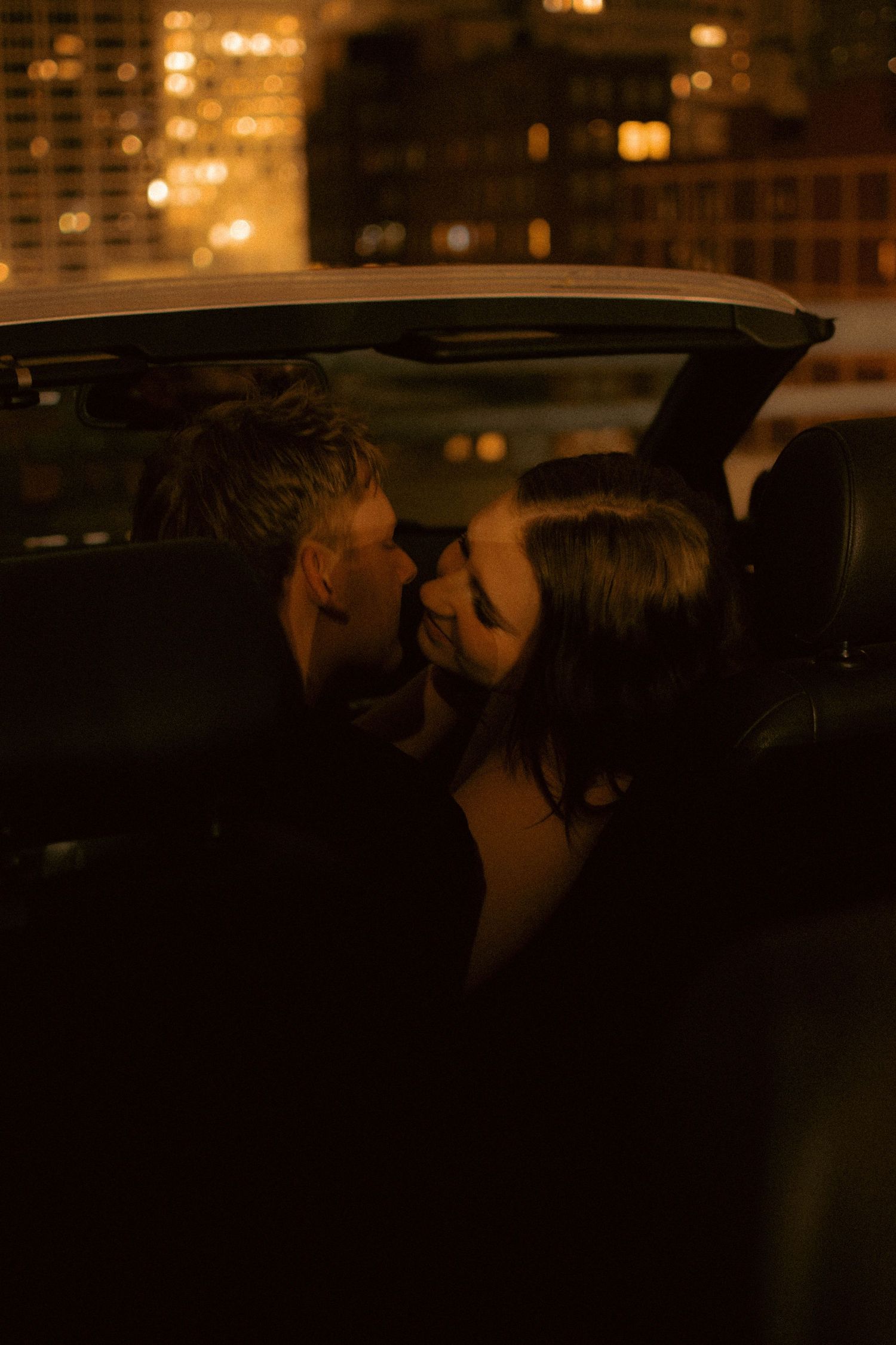 Silhouetted figures in an intimate moment against city lights at night.