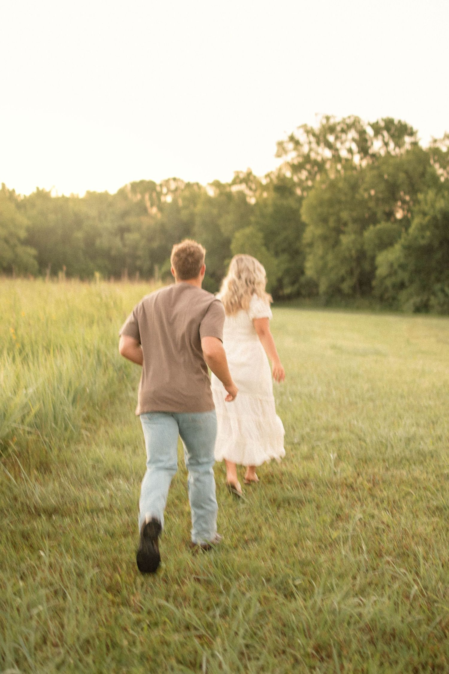 A couple walks hand in hand through a sunlit meadow during golden hour.