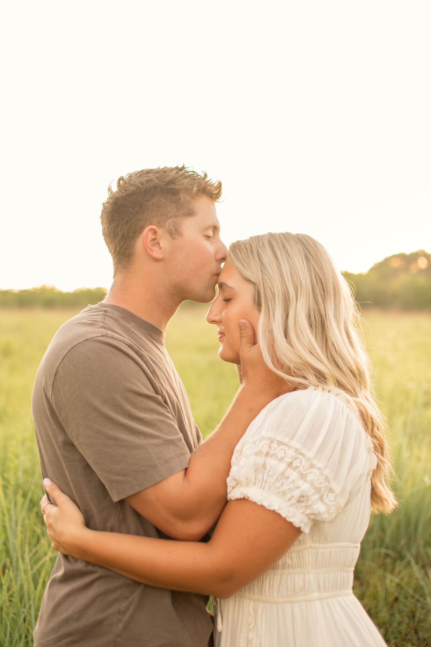 Romantic couple embraces in a golden field at sunset wearing casual attire.