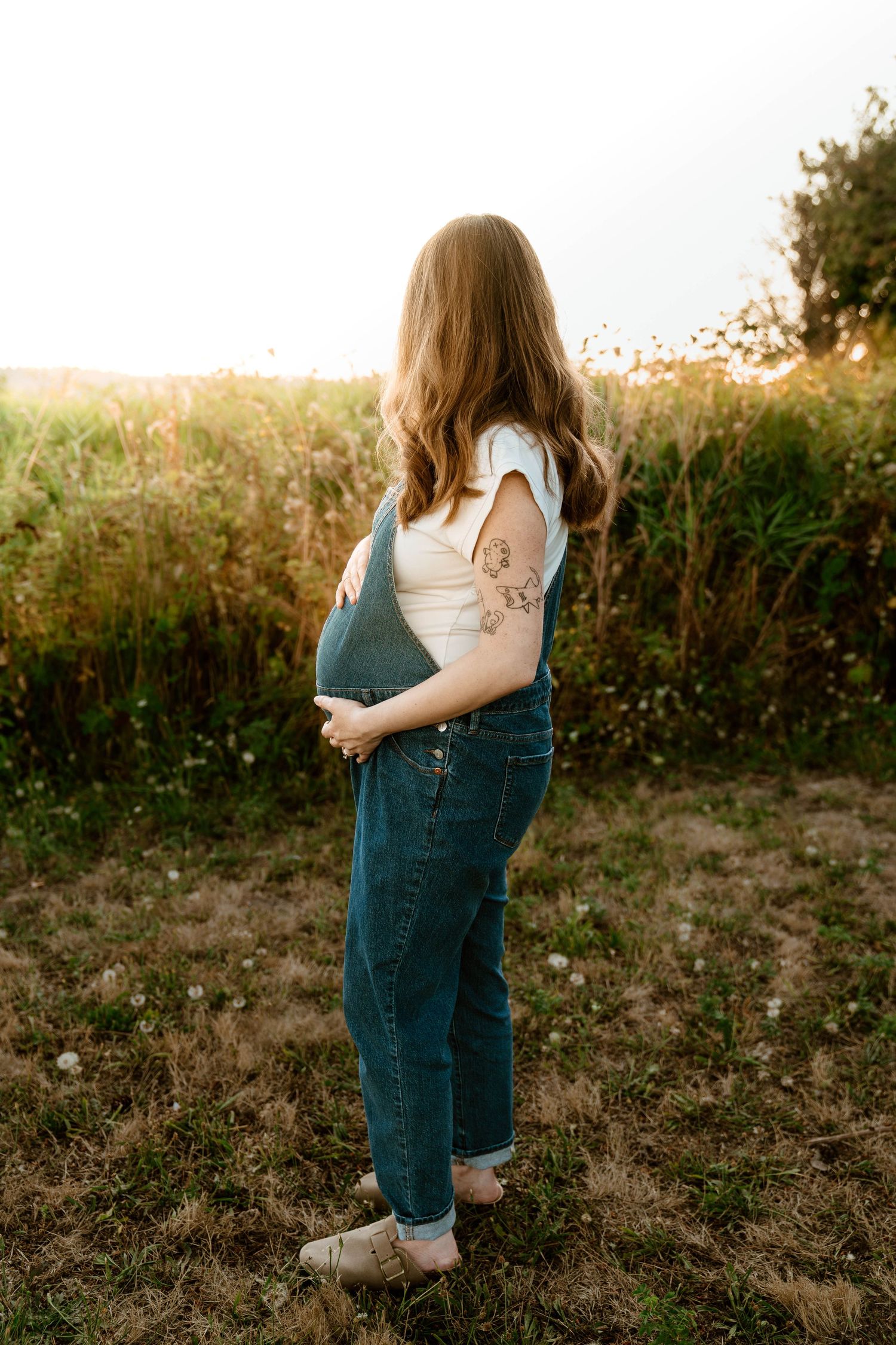 Figure in denim overalls standing in golden sunlit field.