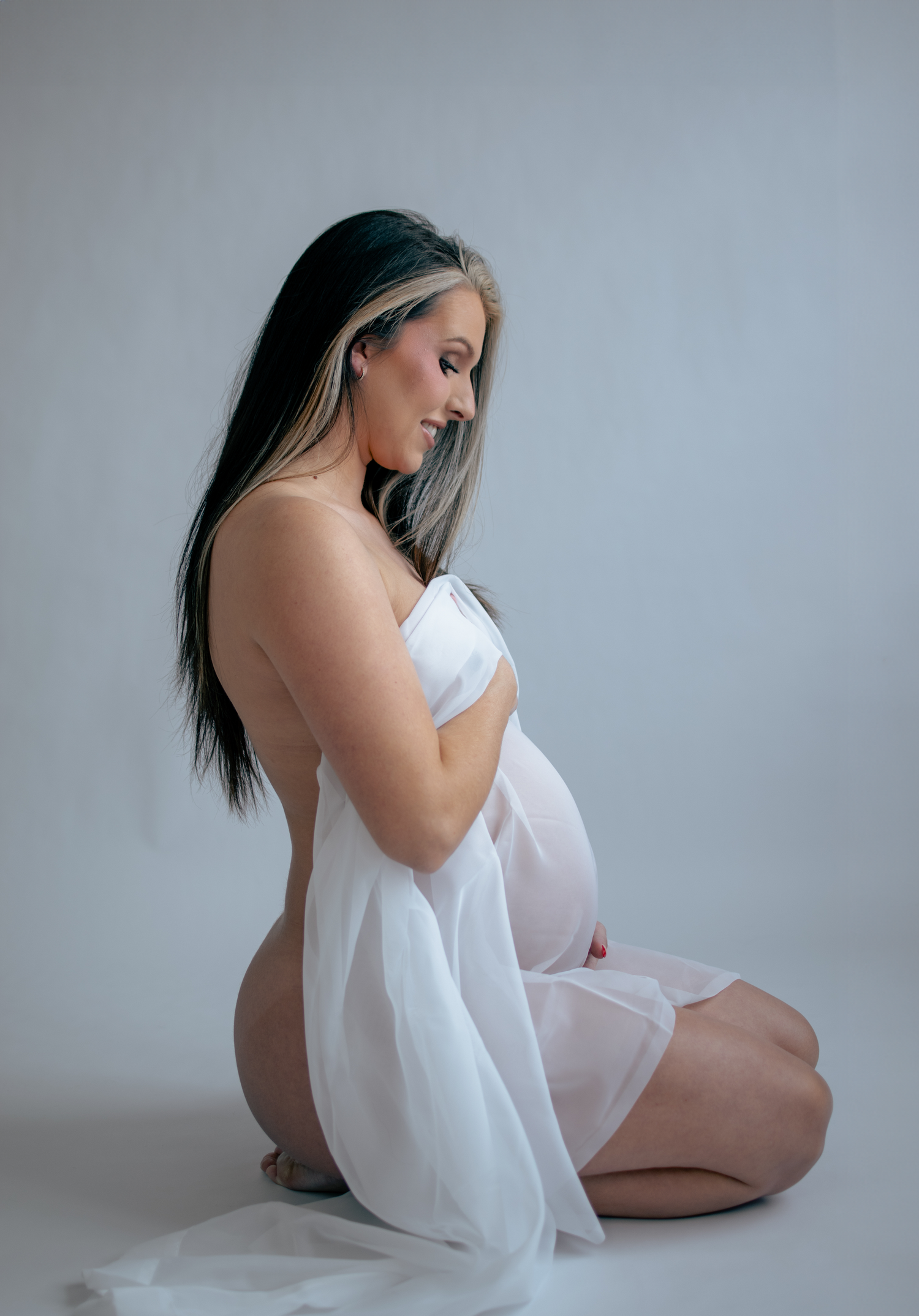 Artistic maternity portrait with flowing white fabric in minimalist studio setting.