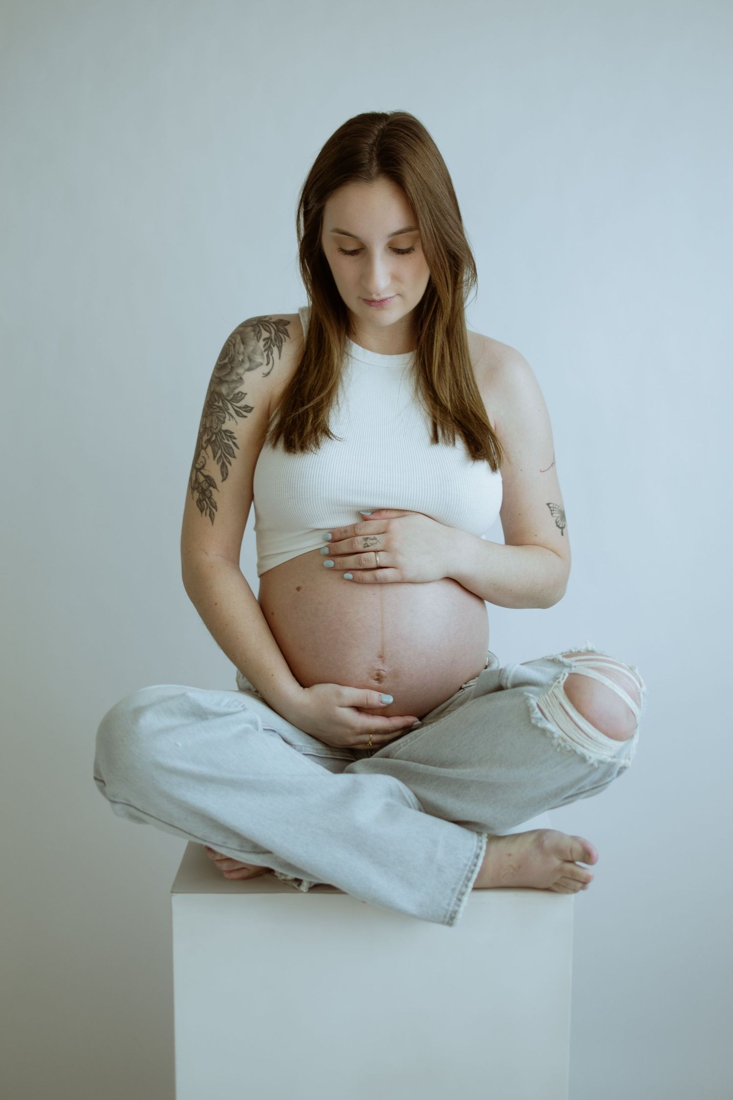 Minimalist maternity portraits showing pregnant woman in white top against light background.