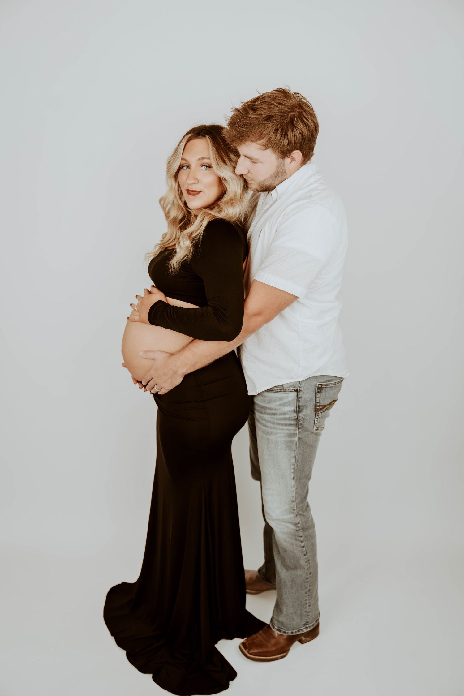 A maternity photo of a couple embracing against a white backdrop.