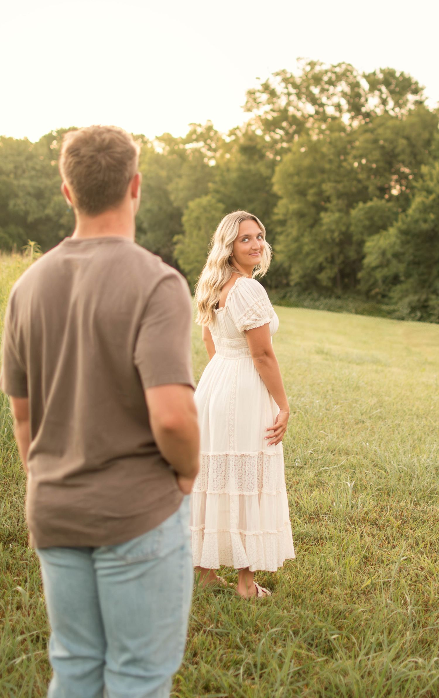 Couple walking together through tall grass in evening sunlight.